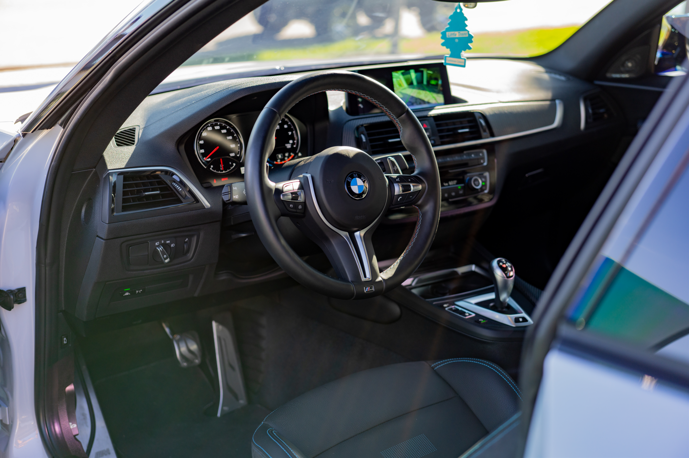 Interior of a BMW car showing the steering wheel, dashboard, digital display, gear shifter, and front seat.