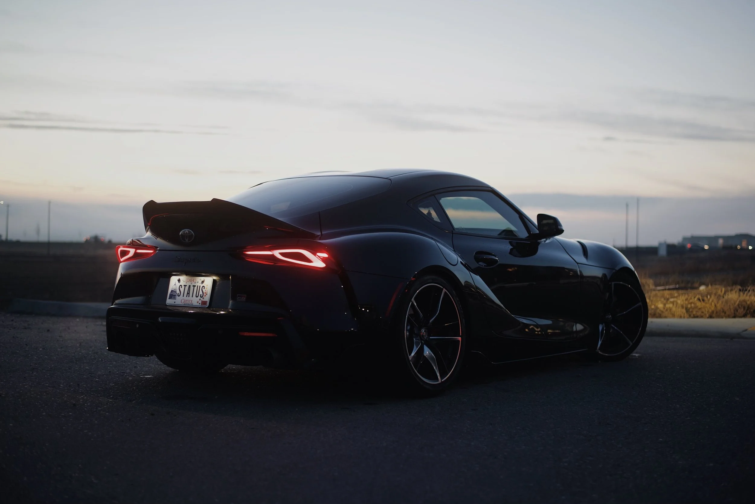 A black sports car parked on the side of the road during dusk, with sleek design and illuminated taillights.