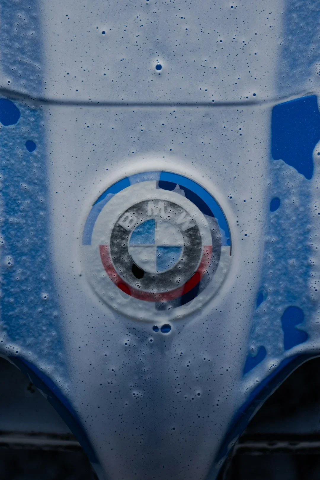 Close-up of a BMW logo on a wet and soap-covered surface, likely a car.