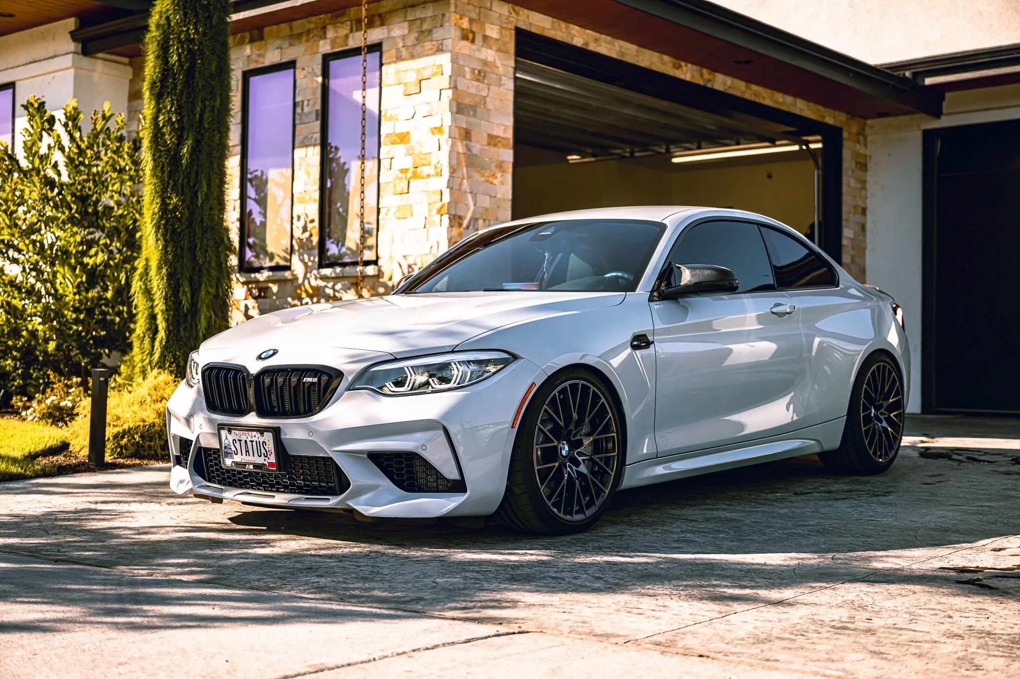 A white BMW coupe parked in front of a modern house with stone and stucco exterior.