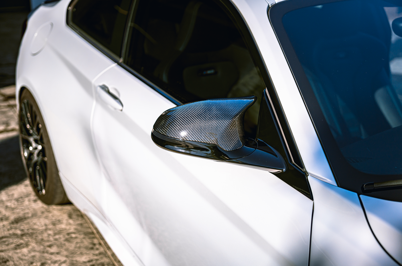 Close-up of a white sports car with a black carbon fiber side mirror.