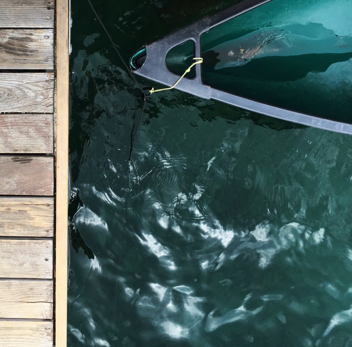 A boat tied to a dock with a rope, floating in water near a wooden pier.