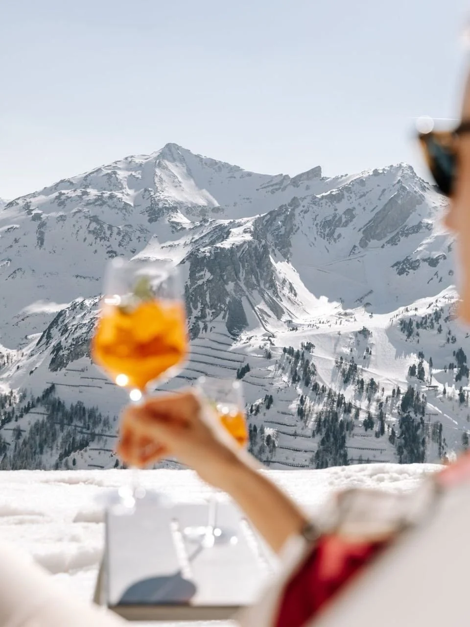 person drinking cocktail with view of white capped mountains