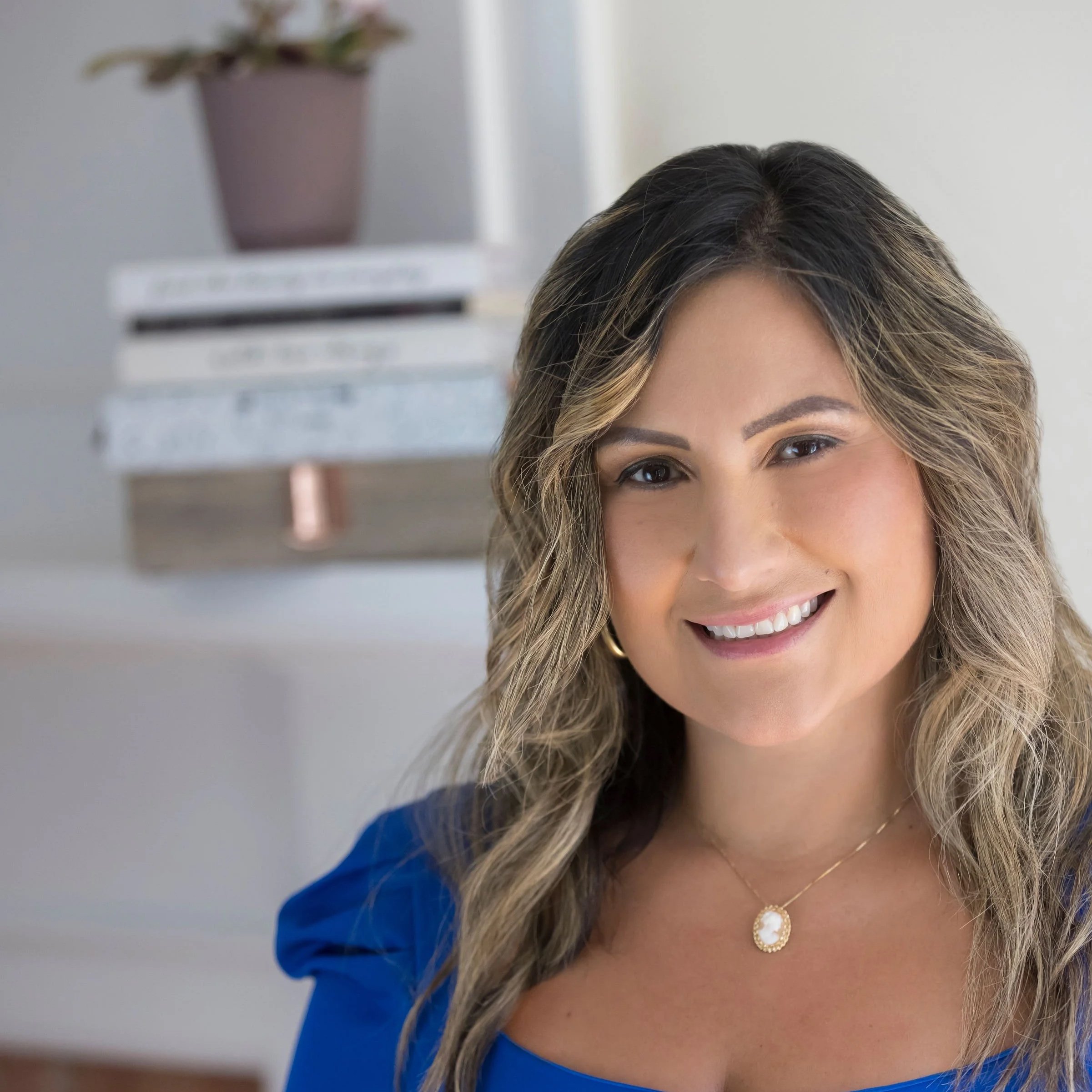 A woman with long, wavy brown hair and wearing a blue top, smiling at the camera.