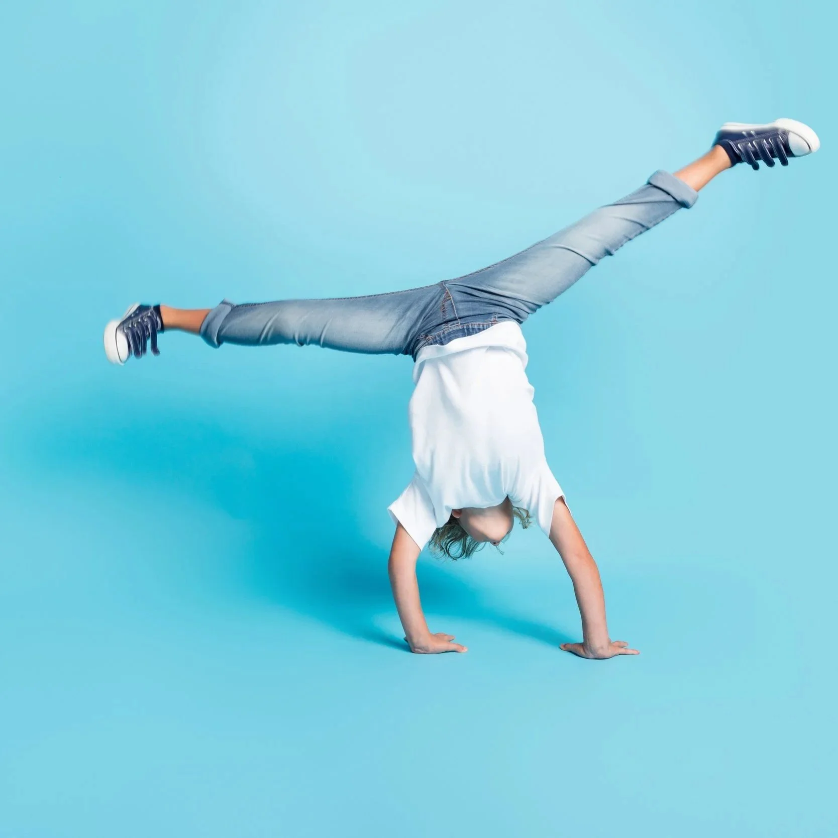 Person performing a handstand in a well-lit studio with a blue background.