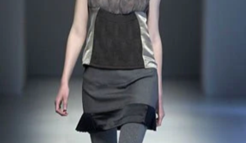 Close-up of a model walking on a runway wearing a gray and black outfit with tights.