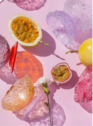 Assorted colorful rocks and a halved passion fruit on a pink background.