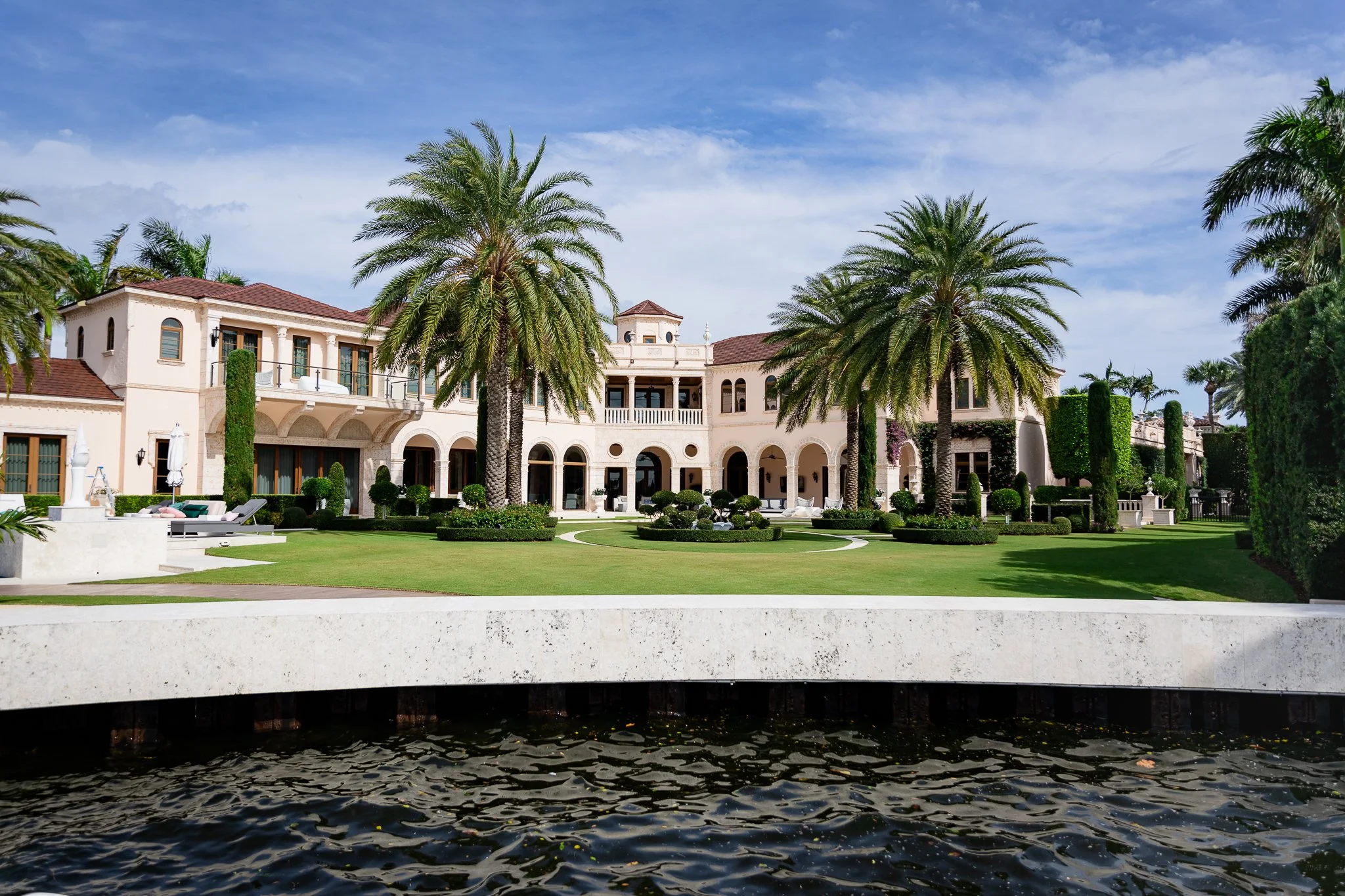 Luxury mansion with palm trees and a waterway in the foreground.