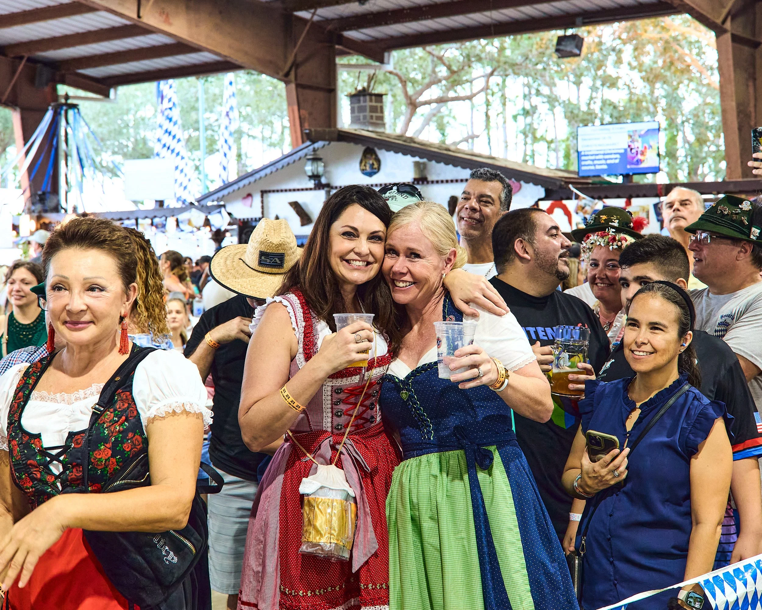 Group of people at a festive event, some wearing traditional German attire like dirndls and hats, in a decorated indoor setting.
