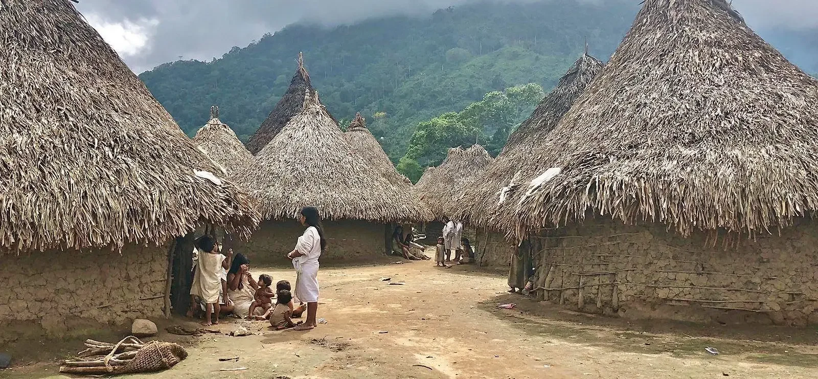 Aldeas tradicionales con casas de barro y techos de palma en un entorno montañoso, con personas indígenas y niños en la plaza central.