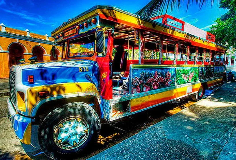 Un autobús turístico colorido, decorado con pintura artística y detalles vibrantes, en una calle soleada.