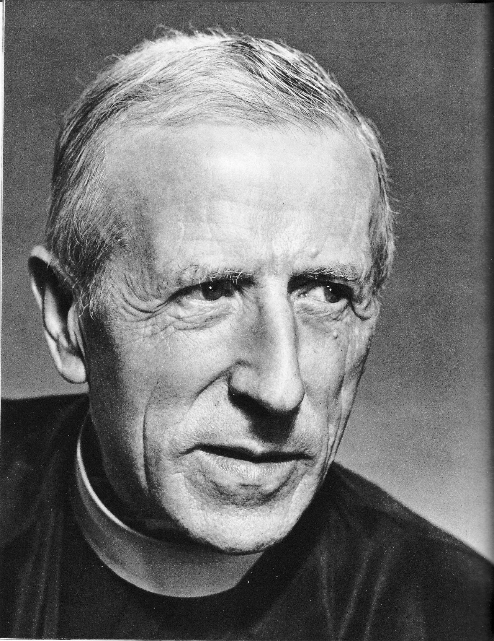 Close-up black and white photograph of an elderly man with short gray hair, wearing clerical attire, looking thoughtfully.