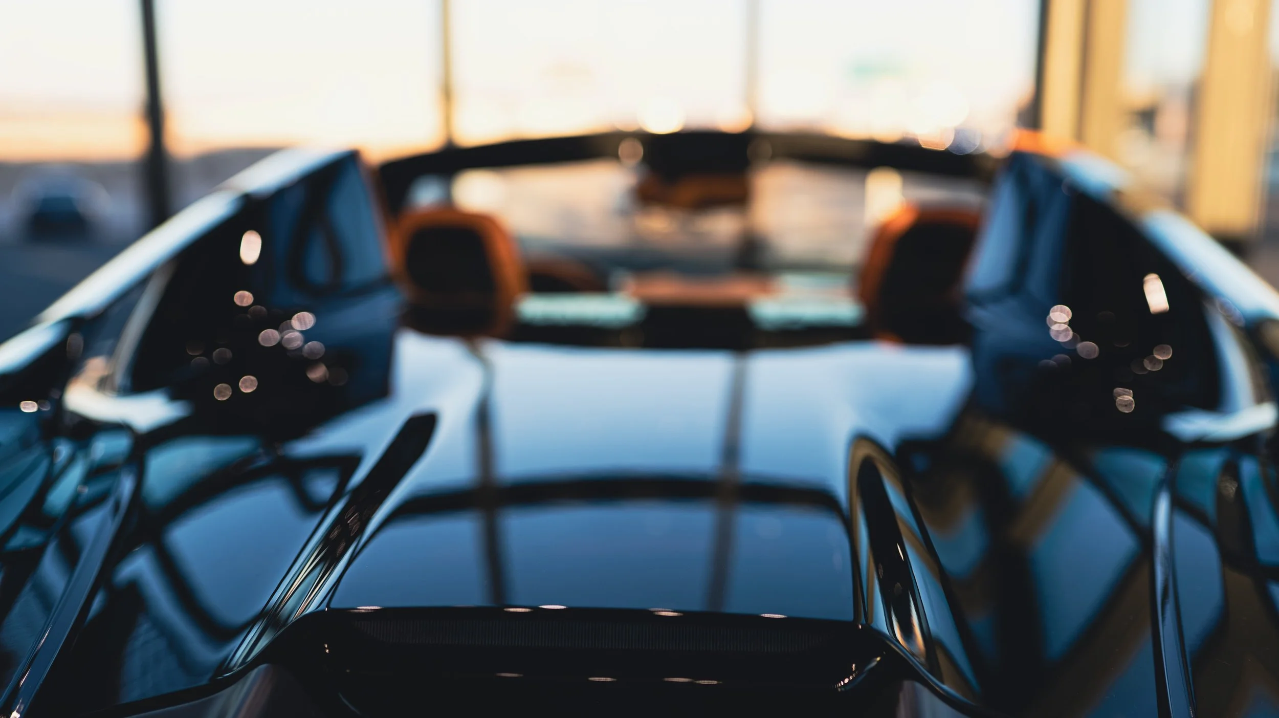 Close-up of a shiny black sports car interior with visible seats and dashboard, reflecting light and surroundings.