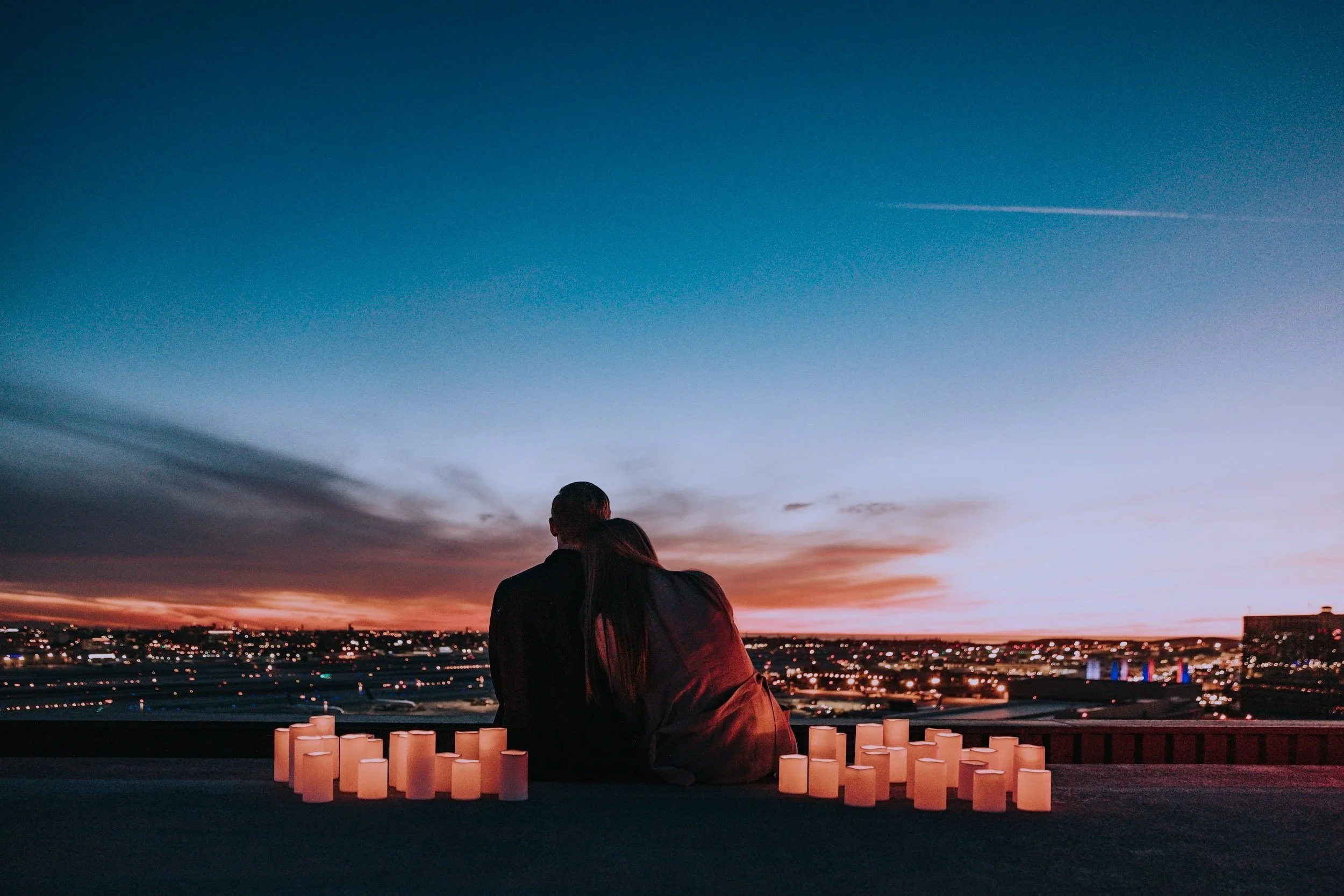 Image of a couple overlooking a city at dusk with candles surrounding them.