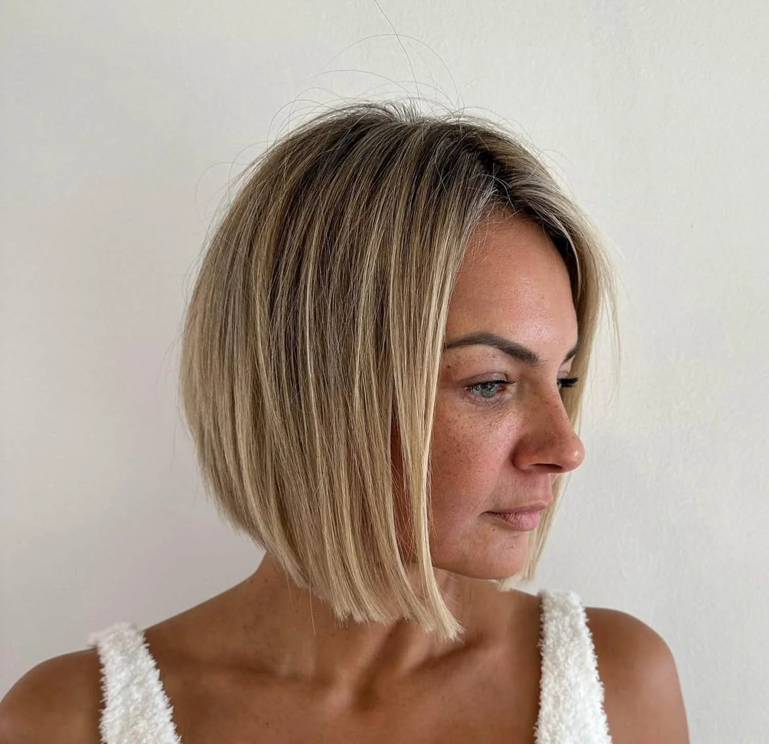 Woman with a short blonde bob haircut, wearing a white fleece top, looking to the right against a plain white wall.