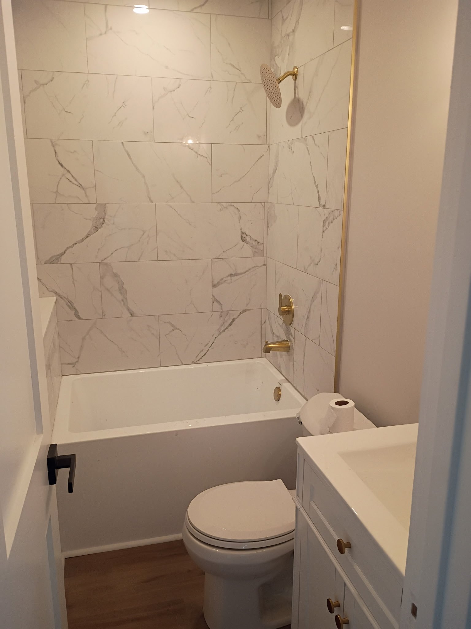 Bathroom with a marble-tiled shower area, a bathtub, a white toilet, and a small white vanity with a sink, featuring gold fixtures.