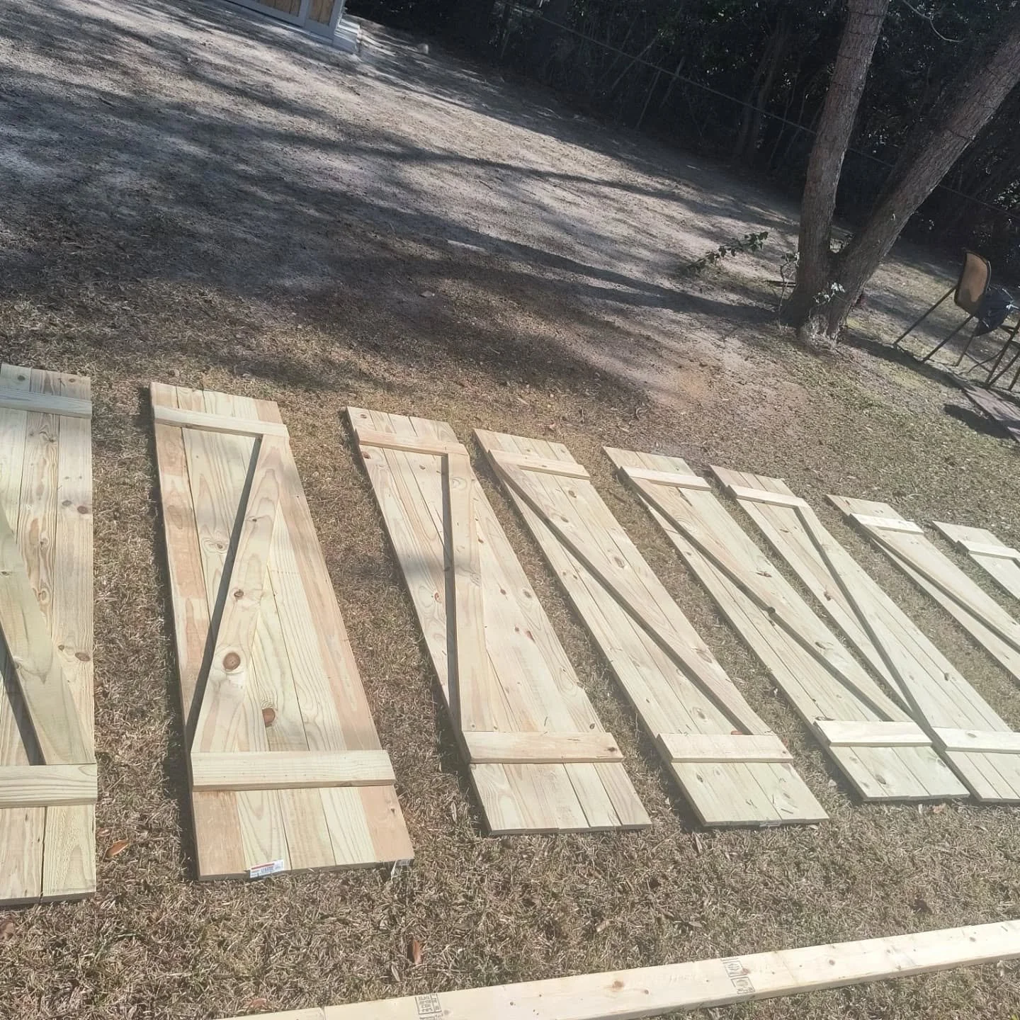Several wooden doors or panels are laid out on the ground outdoors, with a tree and a few chairs in the background.