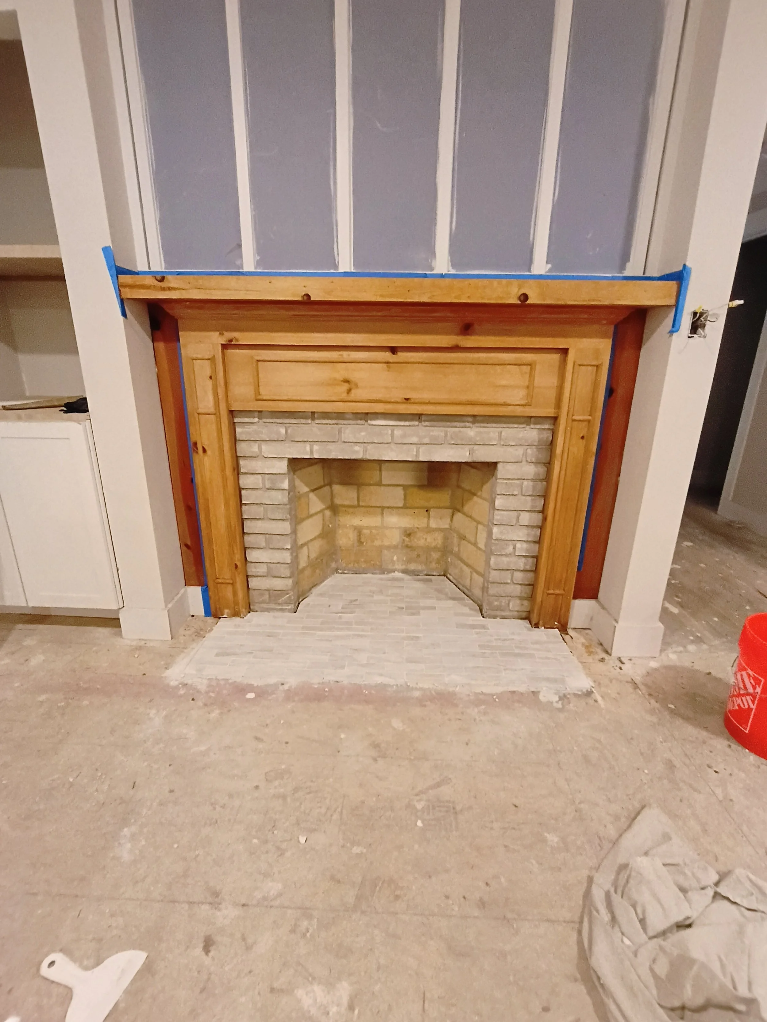 Unfinished fireplace with a brick interior and wooden mantel, surrounded by drywall and construction materials.