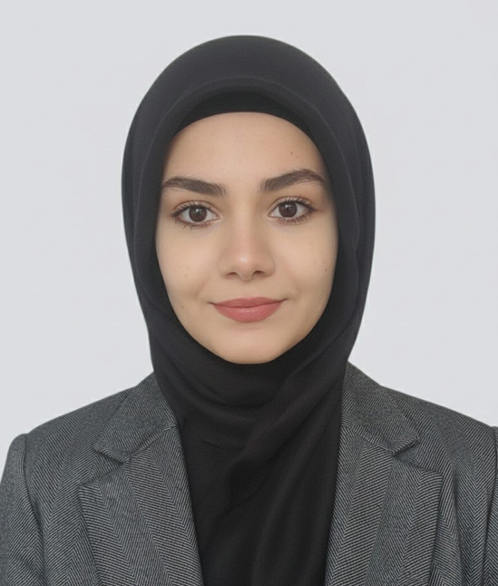 Portrait of a woman wearing a black hijab and gray blazer, smiling softly at the camera.
