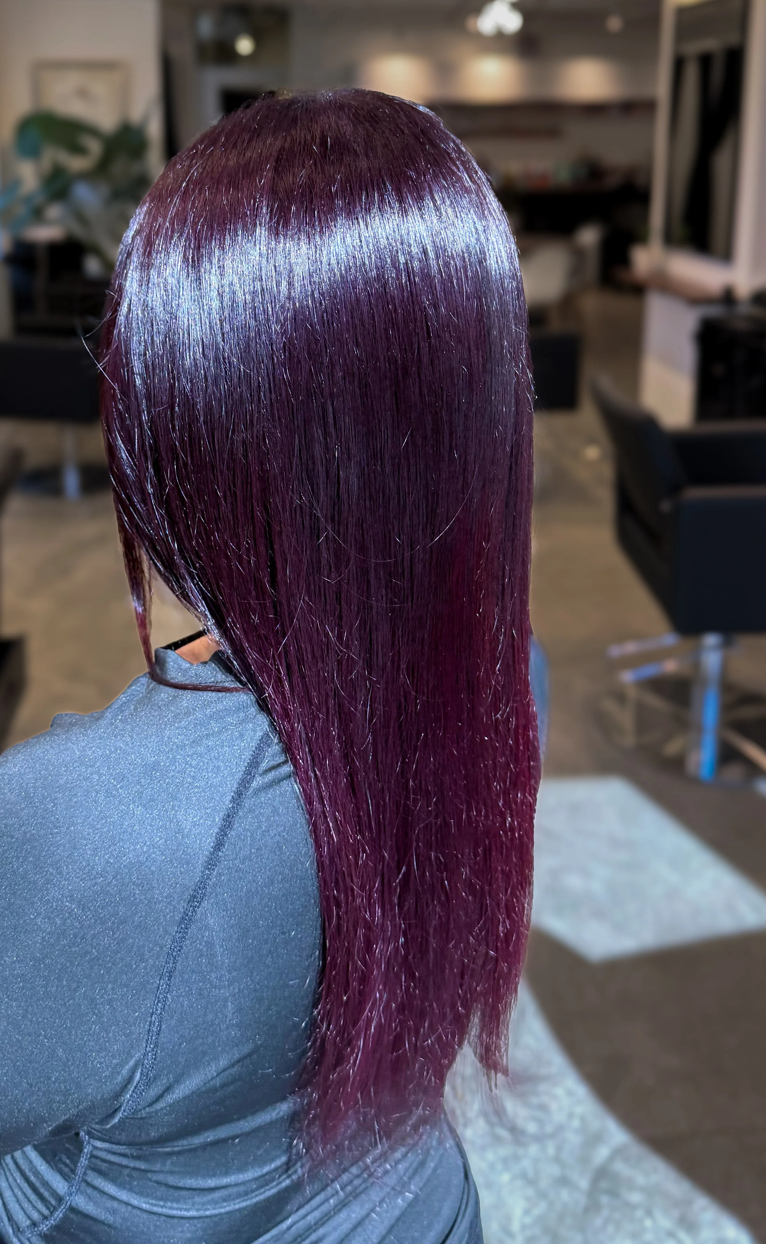 Person with long, shiny, purple and pink hair, sitting in a salon or hair studio.