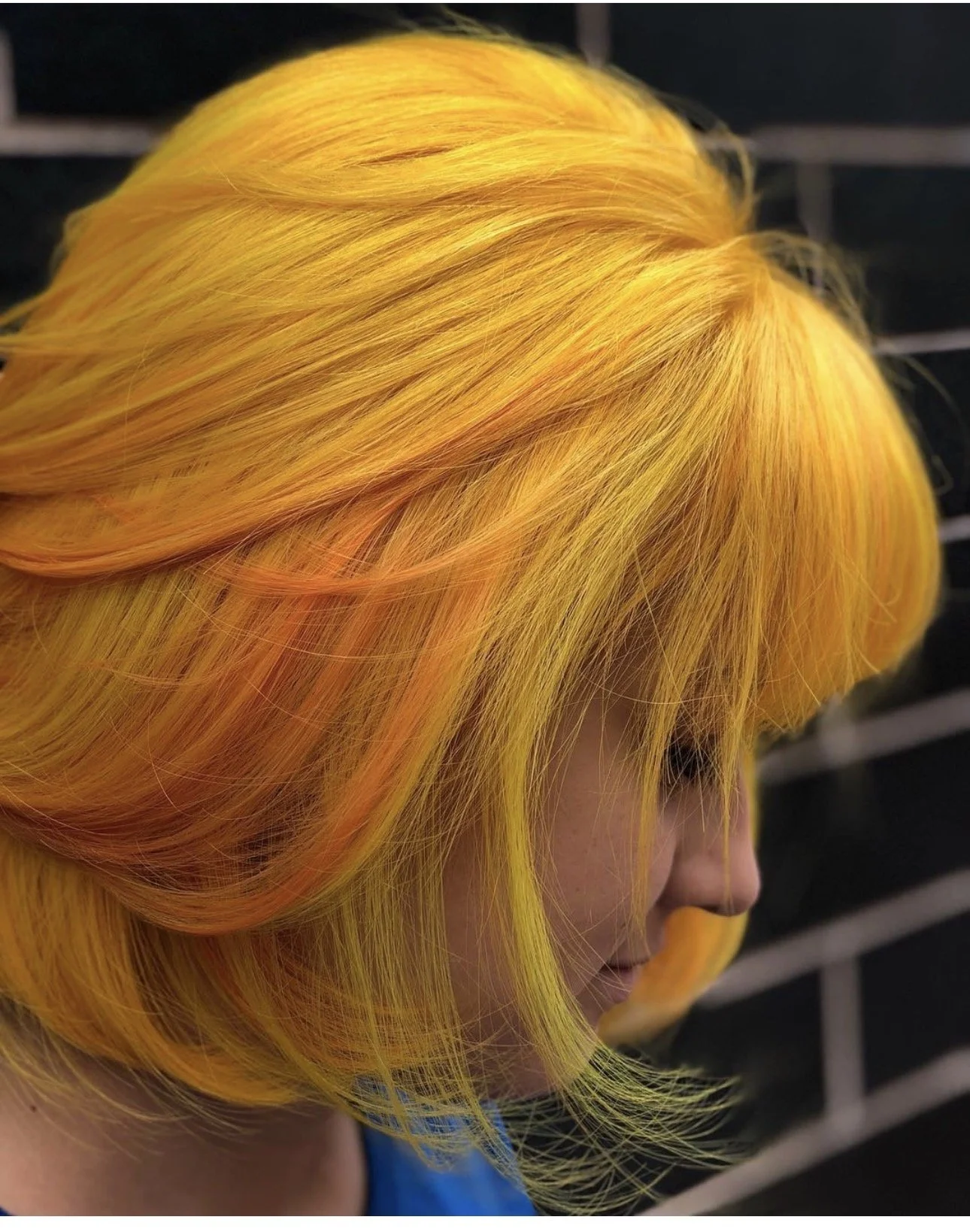 Close-up of a person with bright yellow hair styled in layered, voluminous waves.