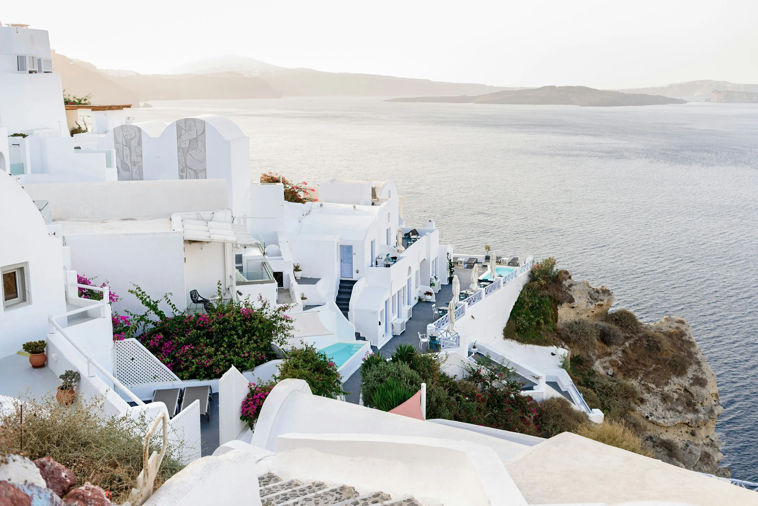 White buildings with blue doors and balconies on a cliff overlooking the sea.