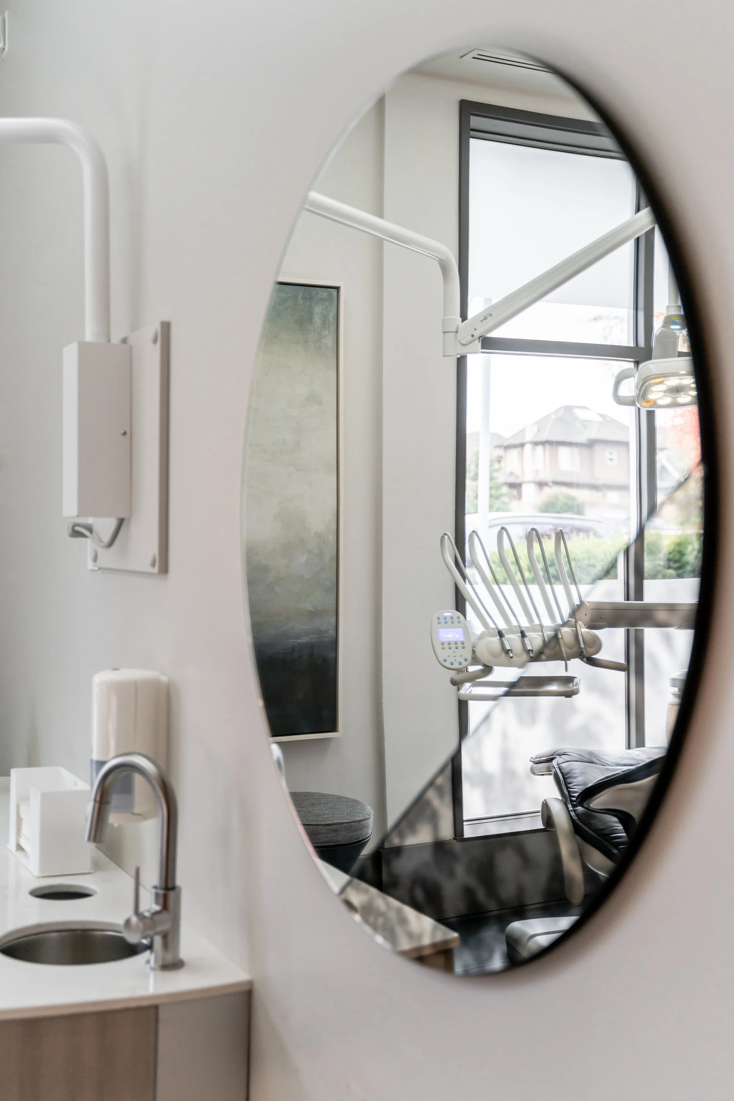 Dental exam room with dental chair, window, mirror, and sink, reflected in a mirror.
