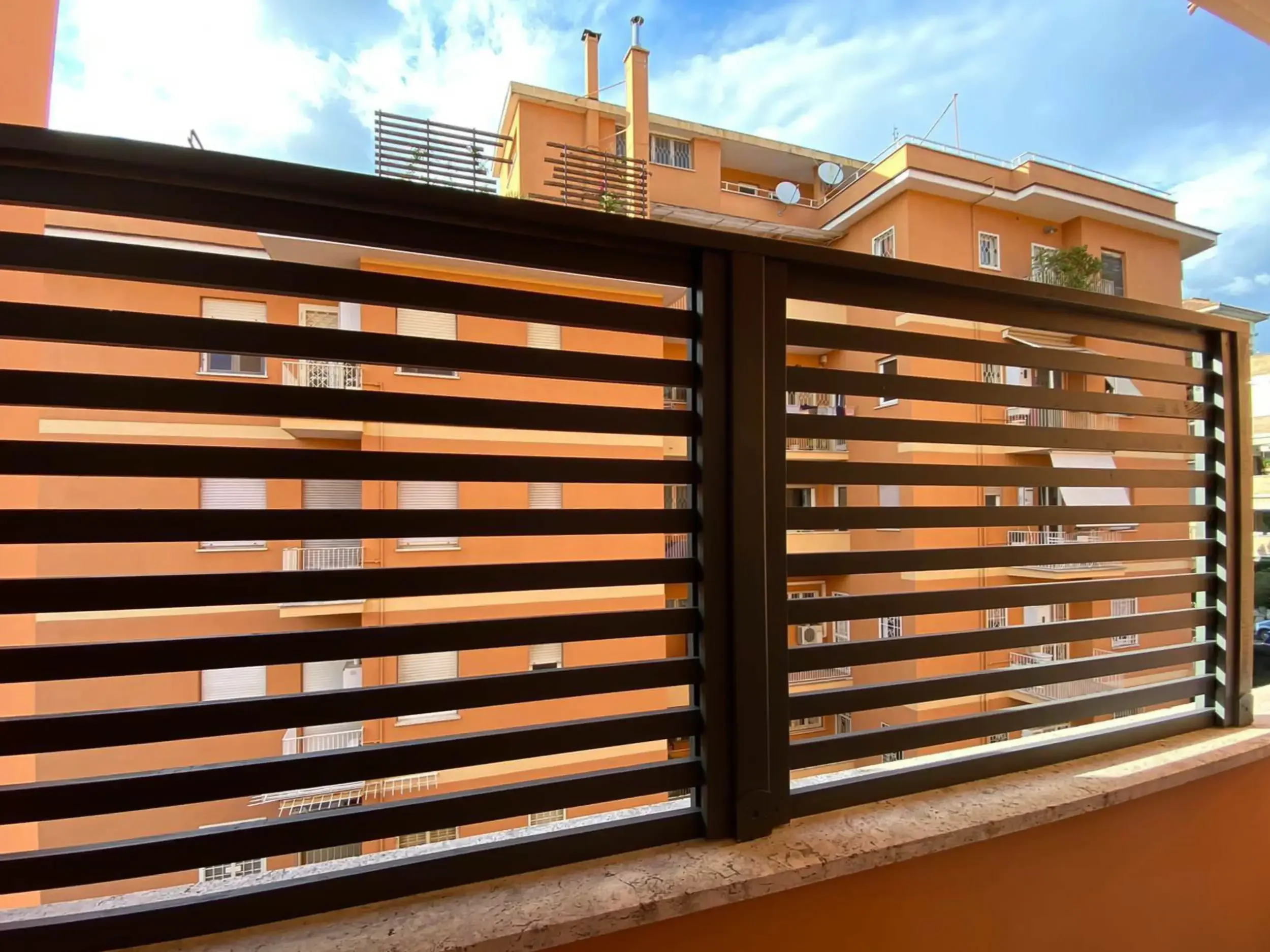 Privacy: Pannelli grigliati orizzontali in metallo marrone per balcone di condominio a Roma.