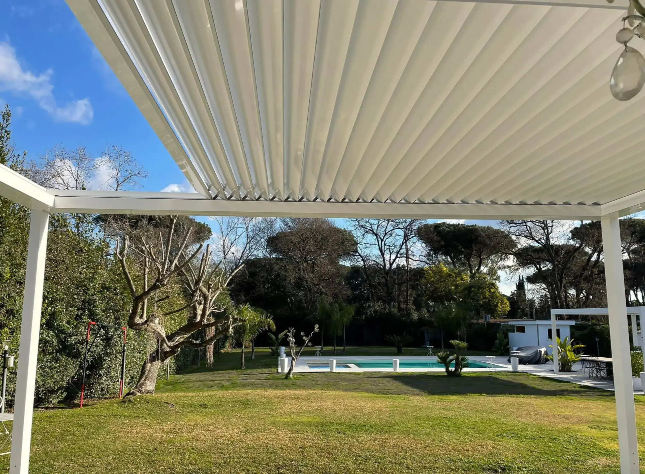 Dettaglio: Le lame lamellari di una pergola bioclimatica bianca durante l'installazione in un giardino.