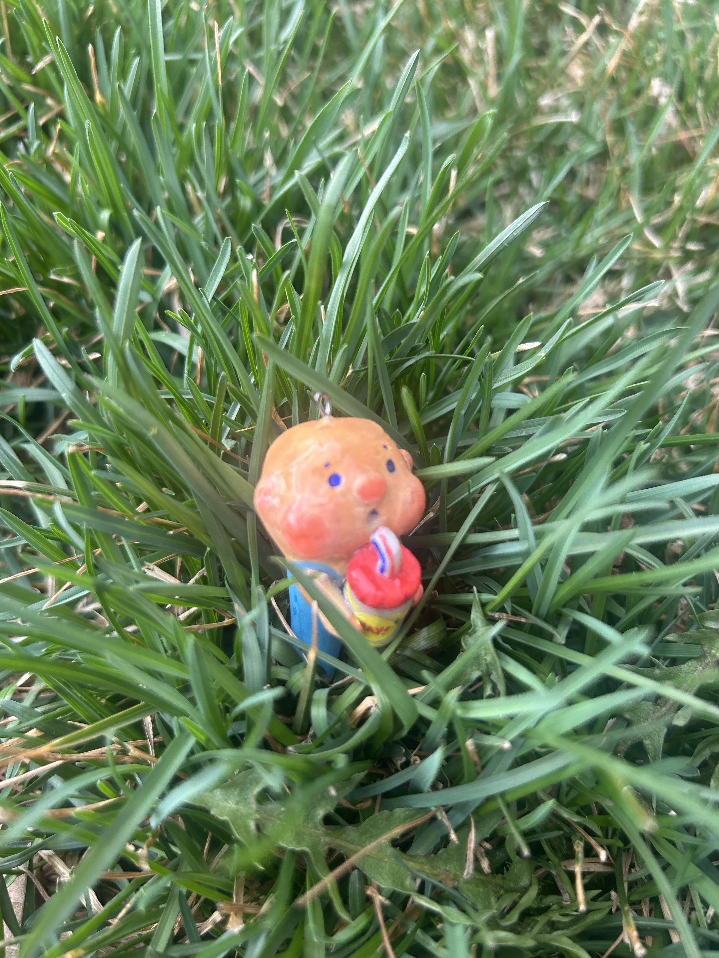 Small figurine of a person holding a red object, partially hidden among green grass.