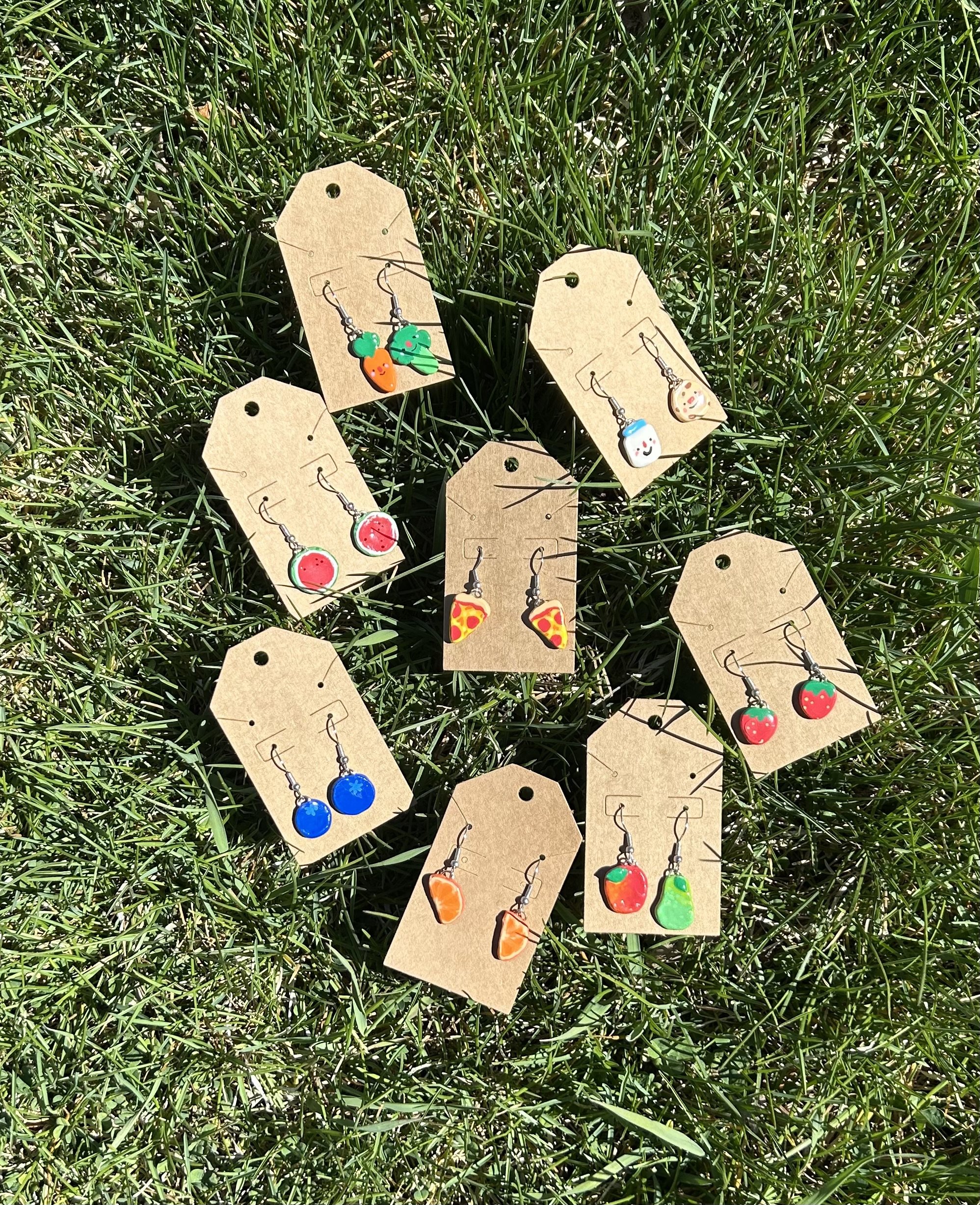 Colorful earrings on brown paper tags laid on green grass.