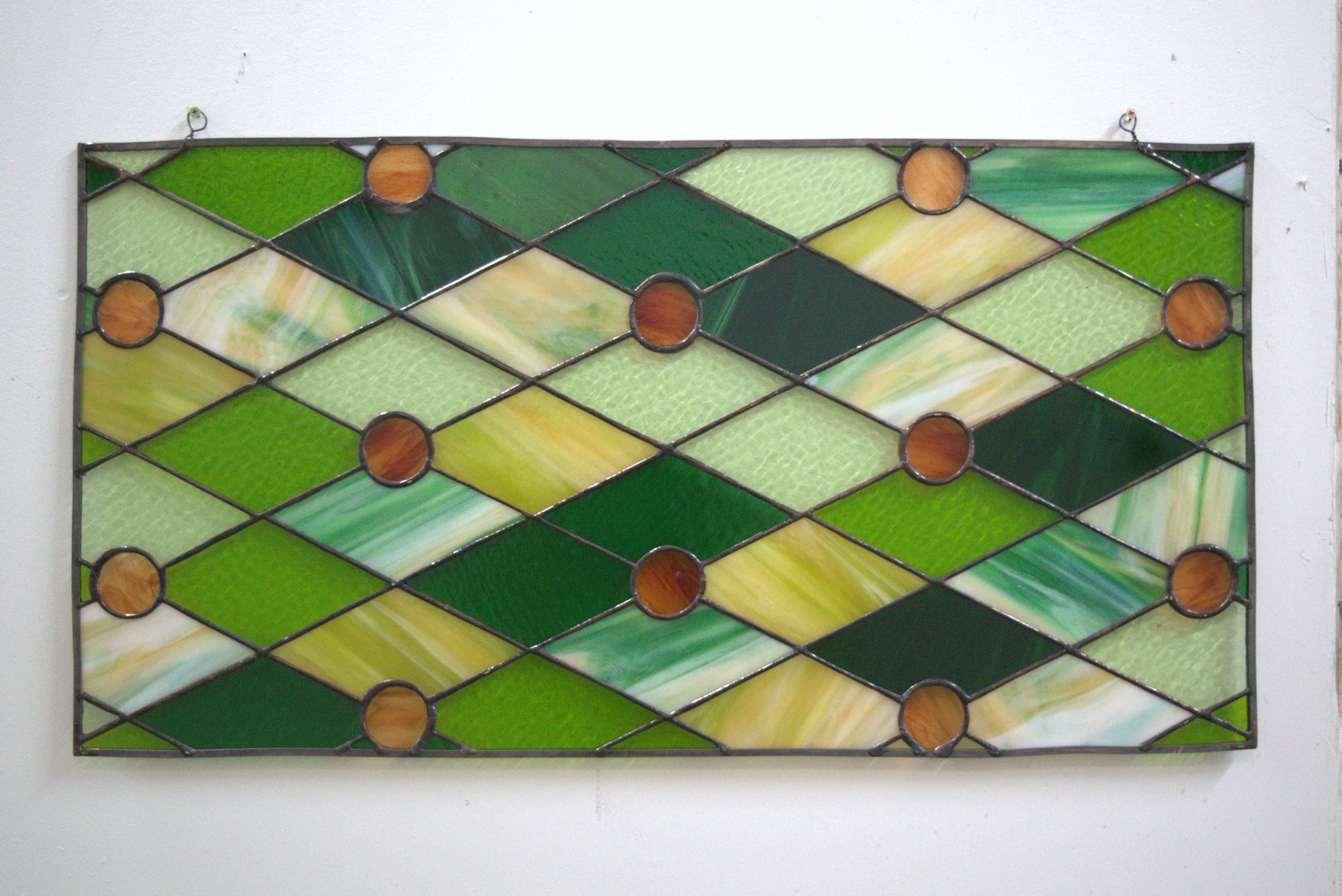 Colorful stained glass wall art with geometric pattern of green, yellow, cream, and brown glass pieces.