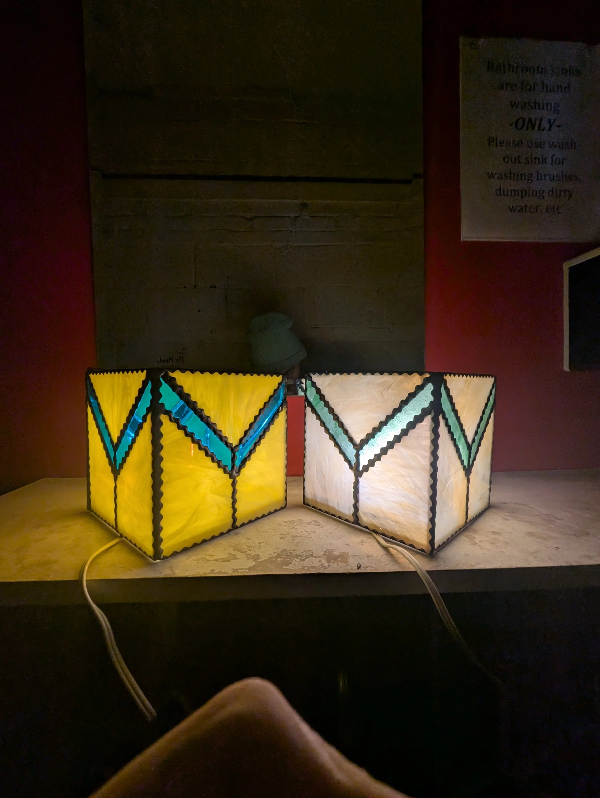Two decorative lamps with stained glass designs on a wooden surface in a dimly lit room.