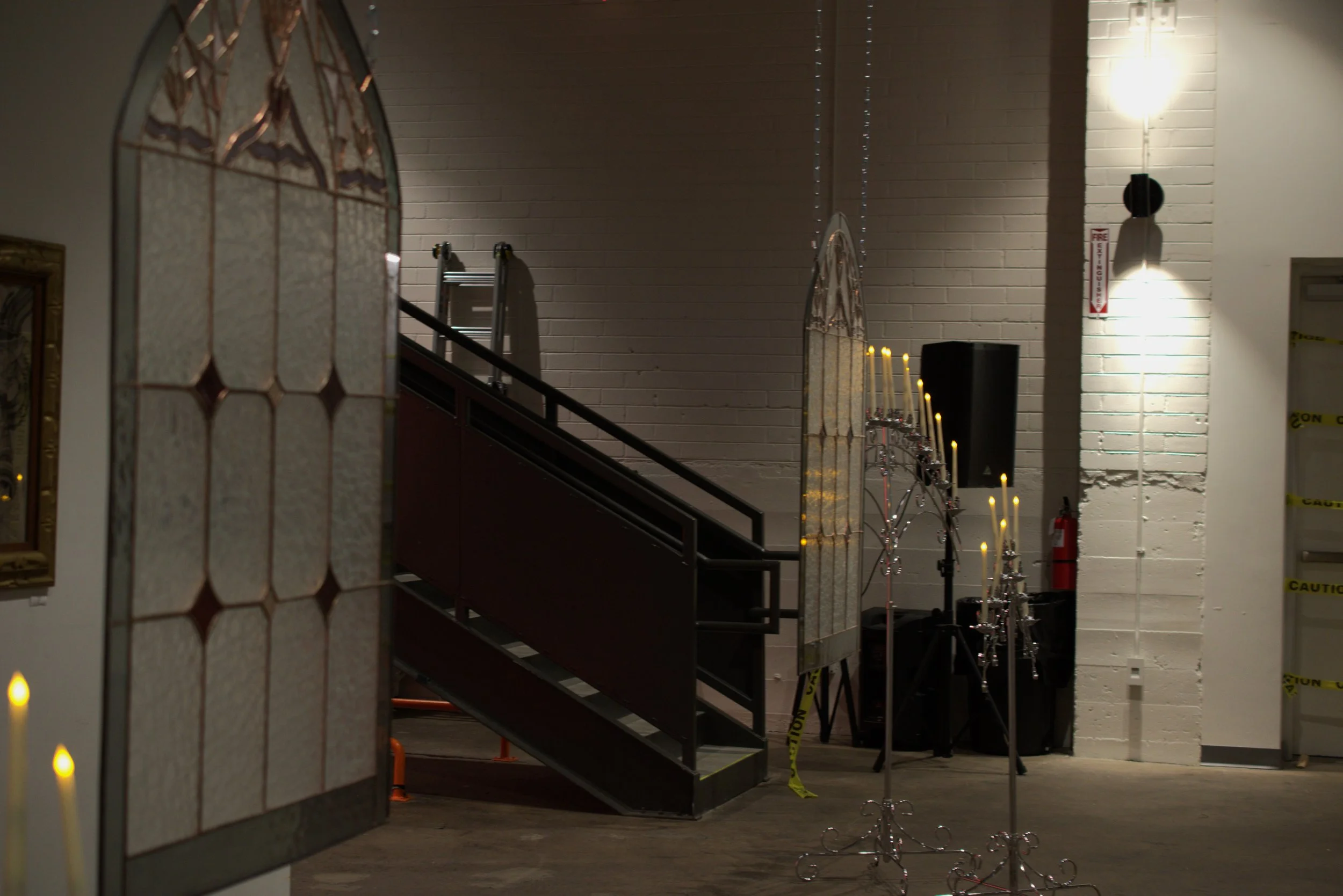 Interior of an event space with white brick walls, lit candles on ornate candelabras, a music speaker, and yellow caution tape.