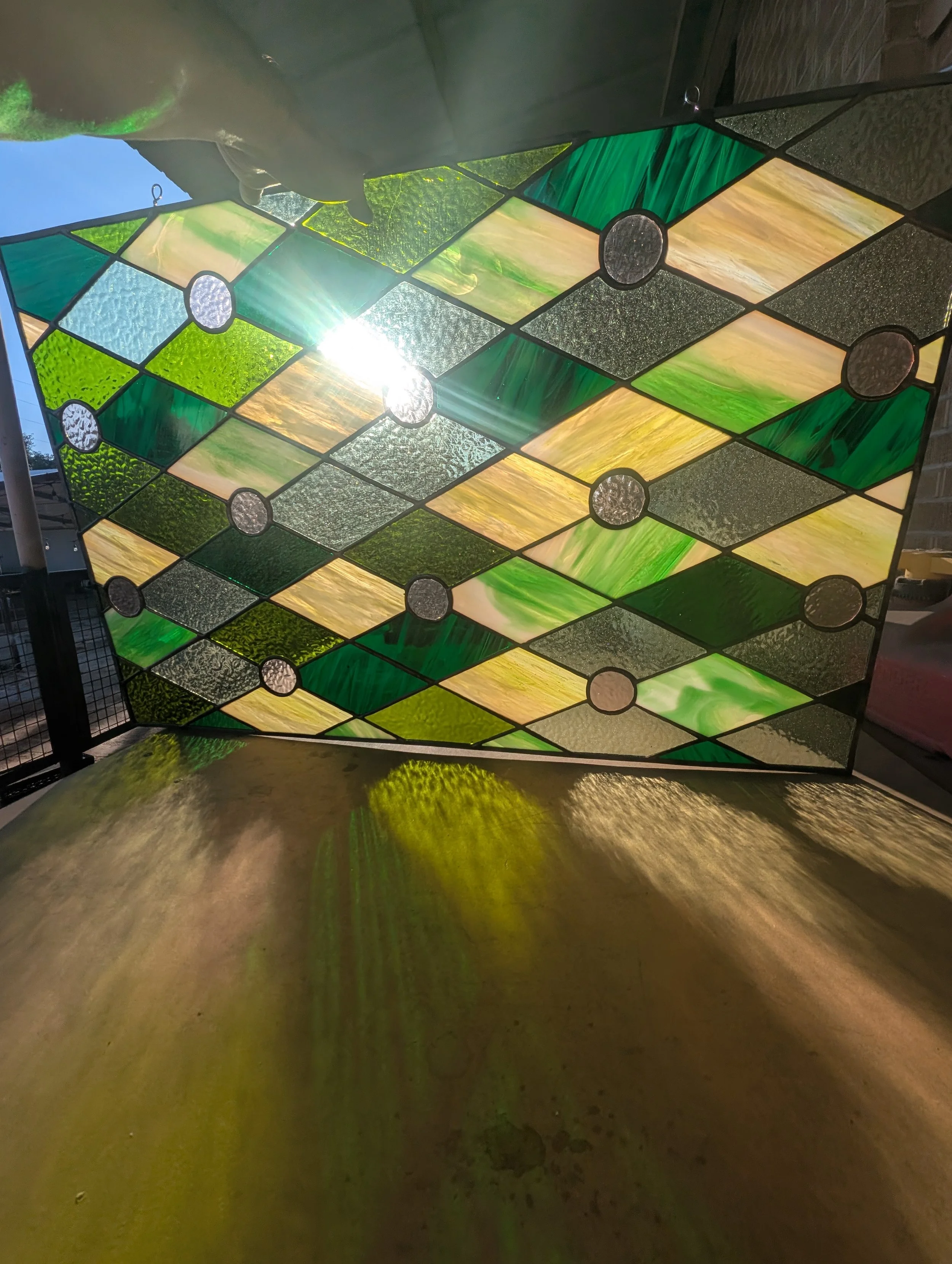 Colorful stained glass window with geometric patterns and sunlight shining through, casting reflections on a surface below.
