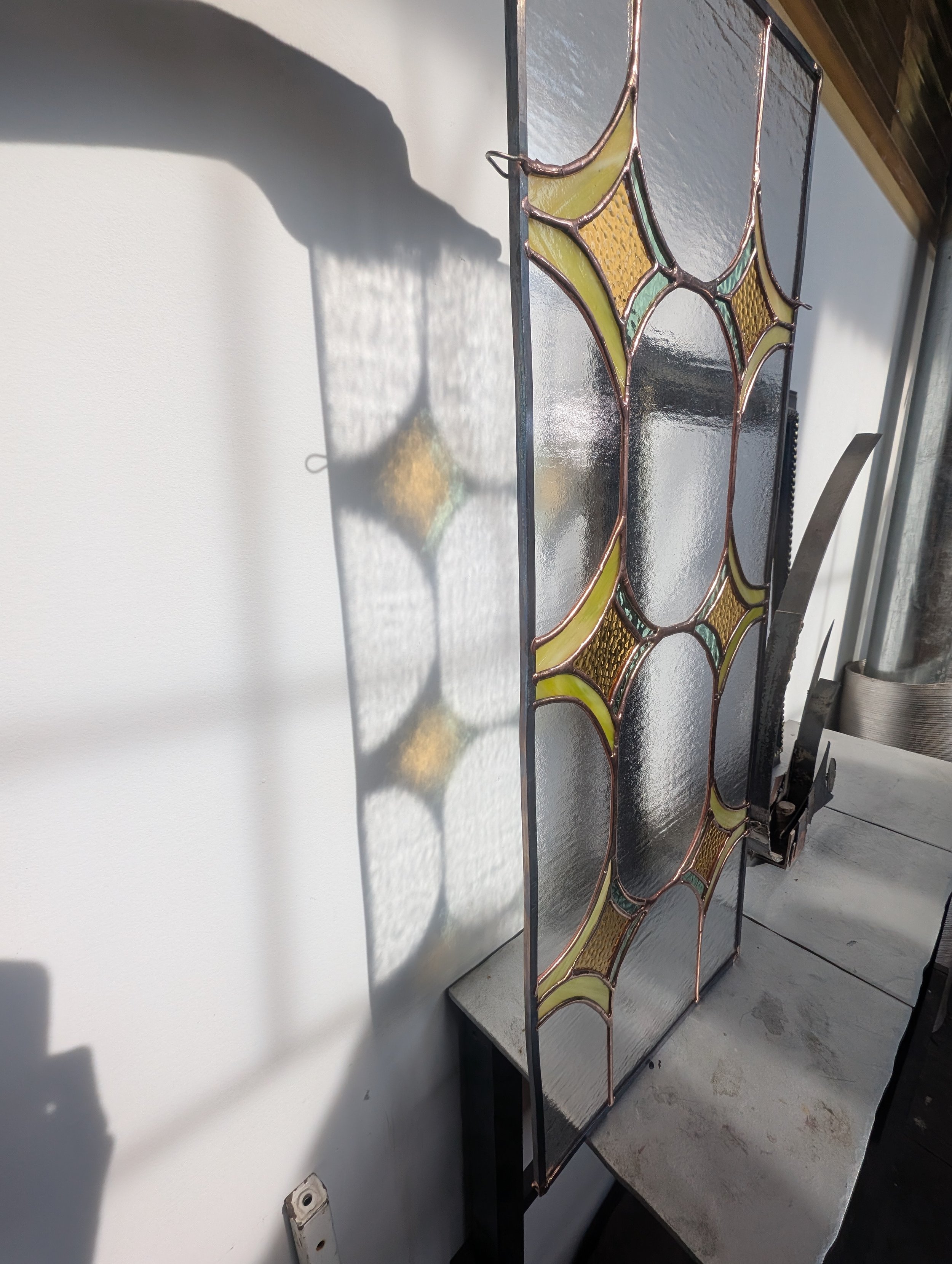 A stained glass window with abstract yellow and brown patterns, casting colorful shadows on a white wall.