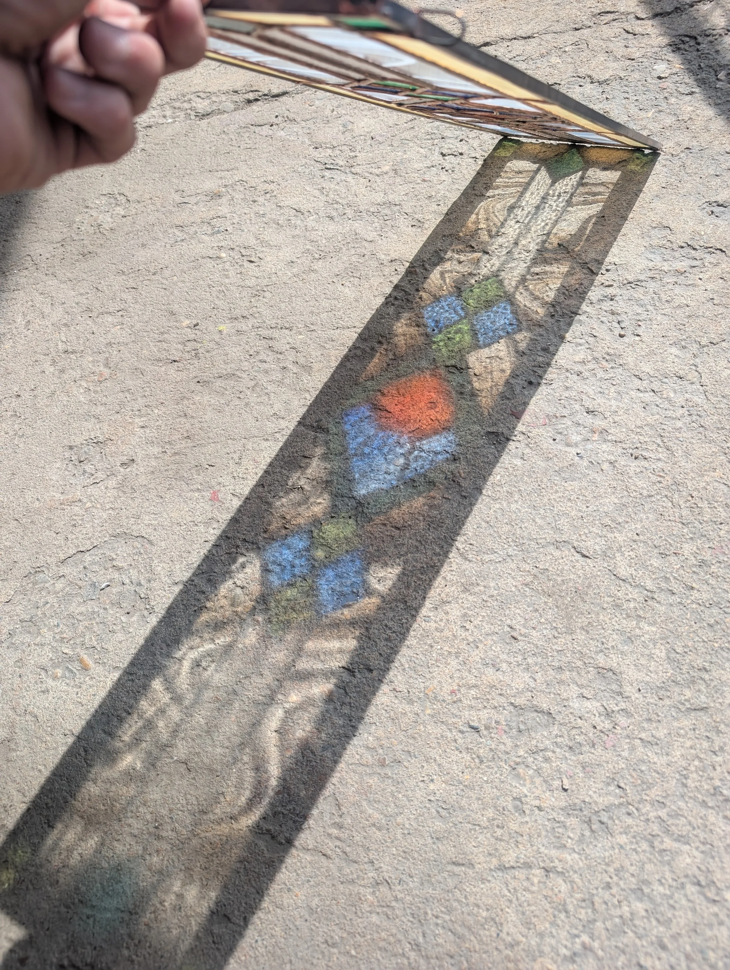 Hand holding a photo creating a shadow on the ground with painting of a colorful theme.