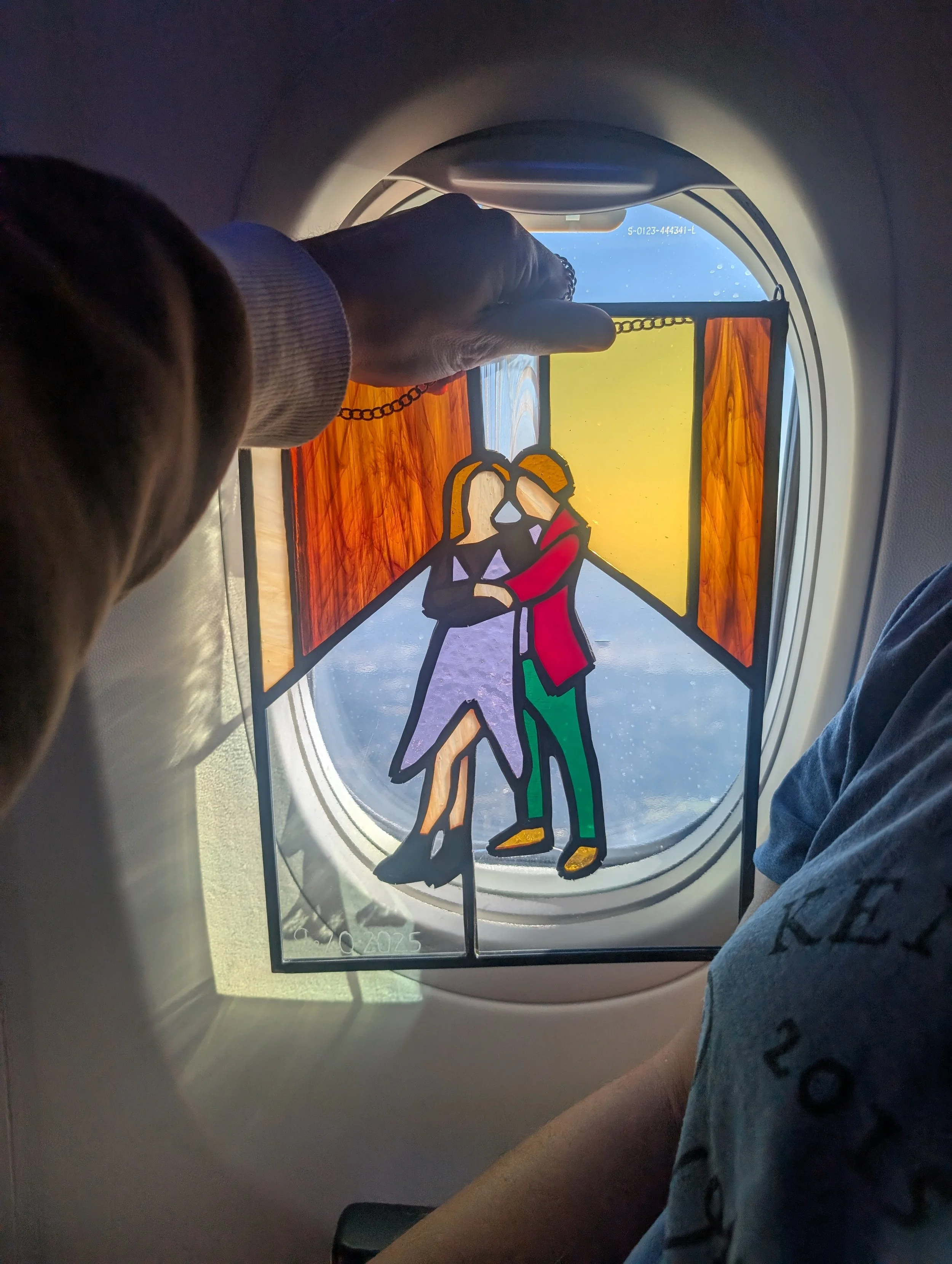 Colorful stained glass window with a scene of two people hugging, viewed from airplane window.