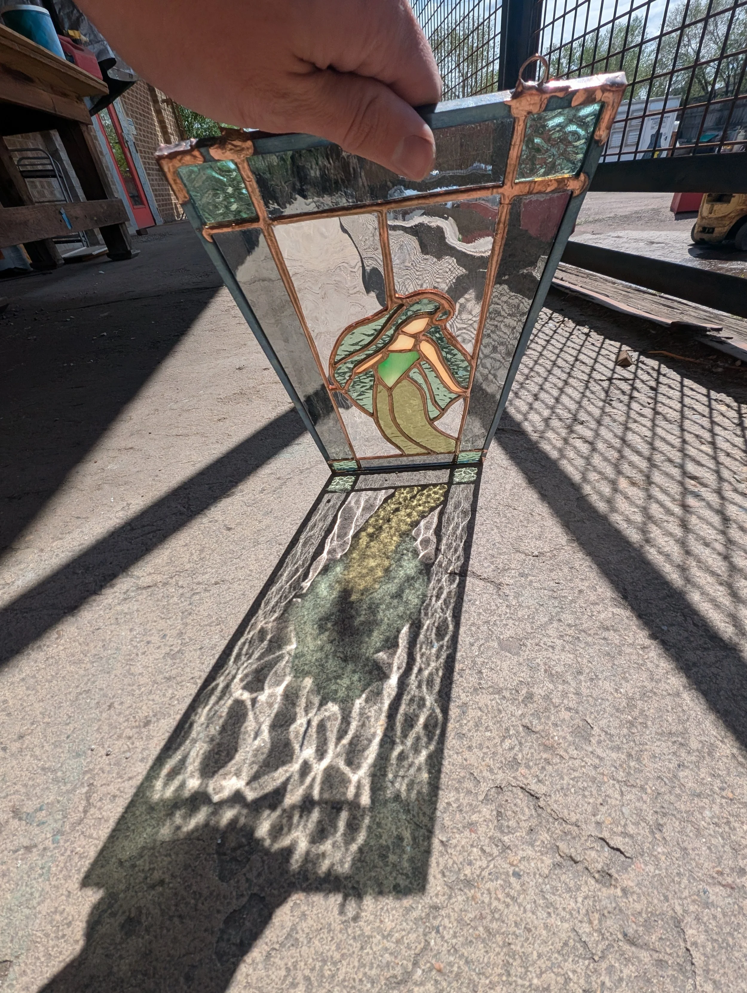 A stained glass lamp with a floral design, held by a hand, casting colorful shadows on the ground.