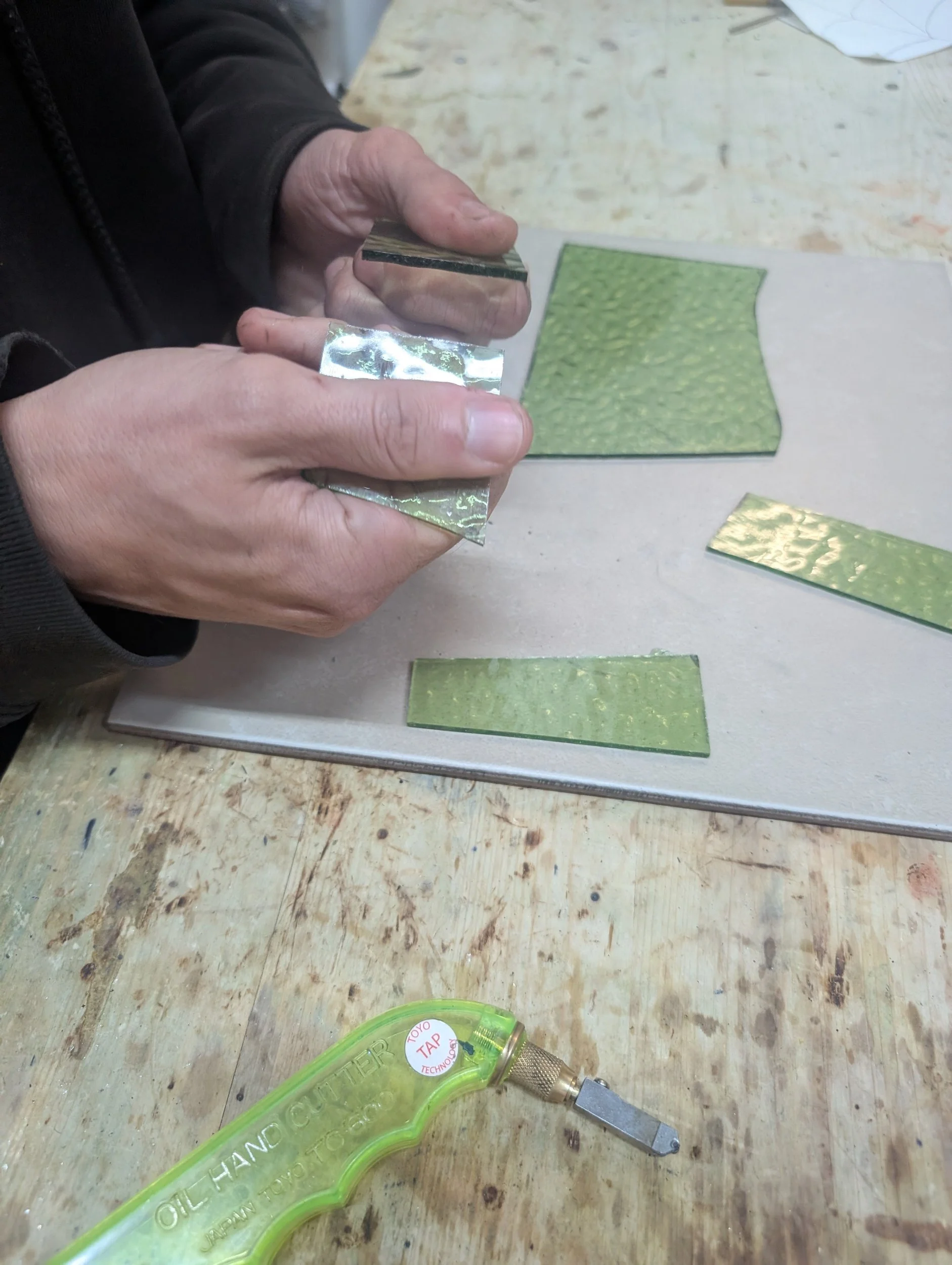 Person working with green textured material and a metal tool on a wooden table.