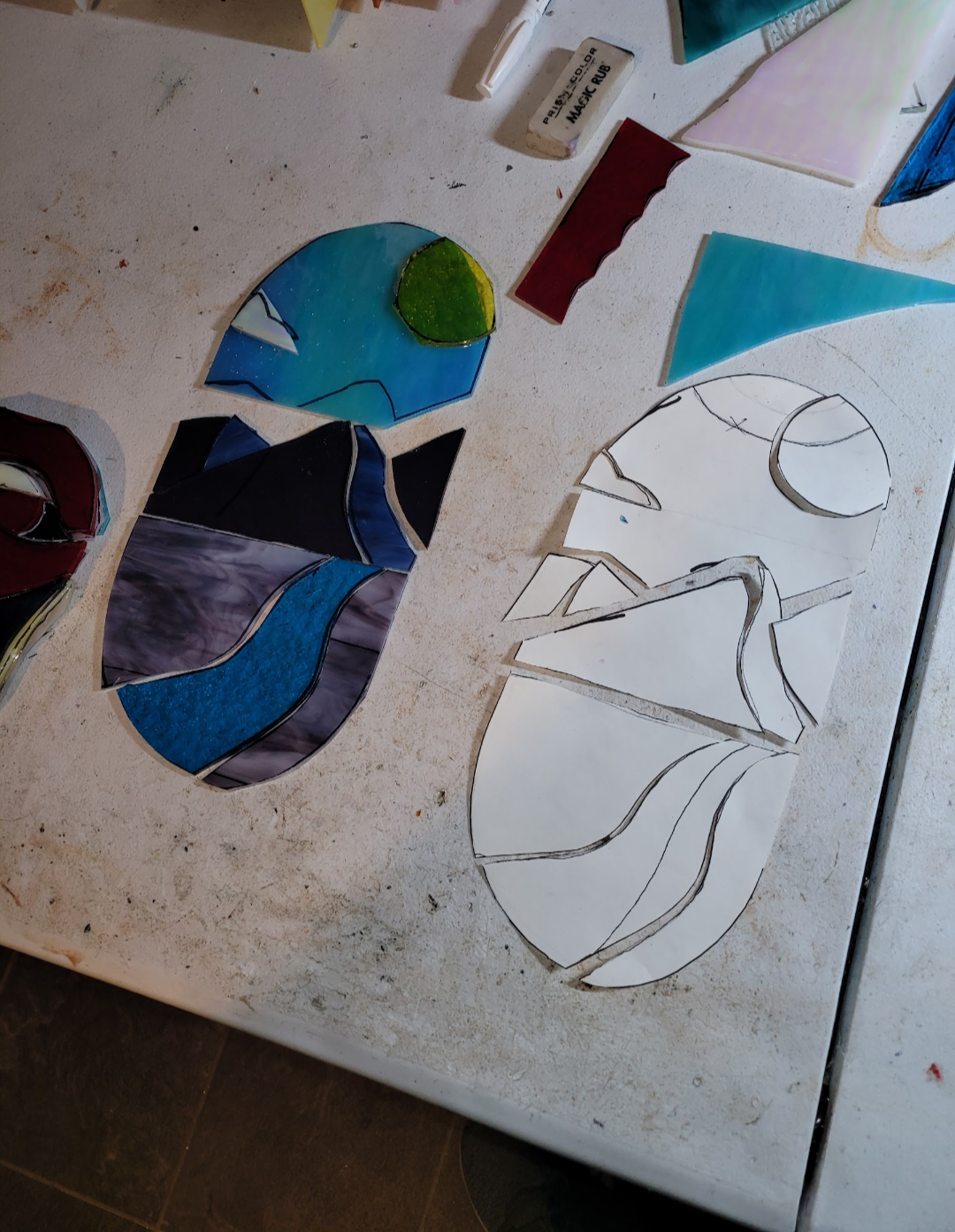 Colorful stained glass pieces and outlines on paper for a mosaic project on a table.