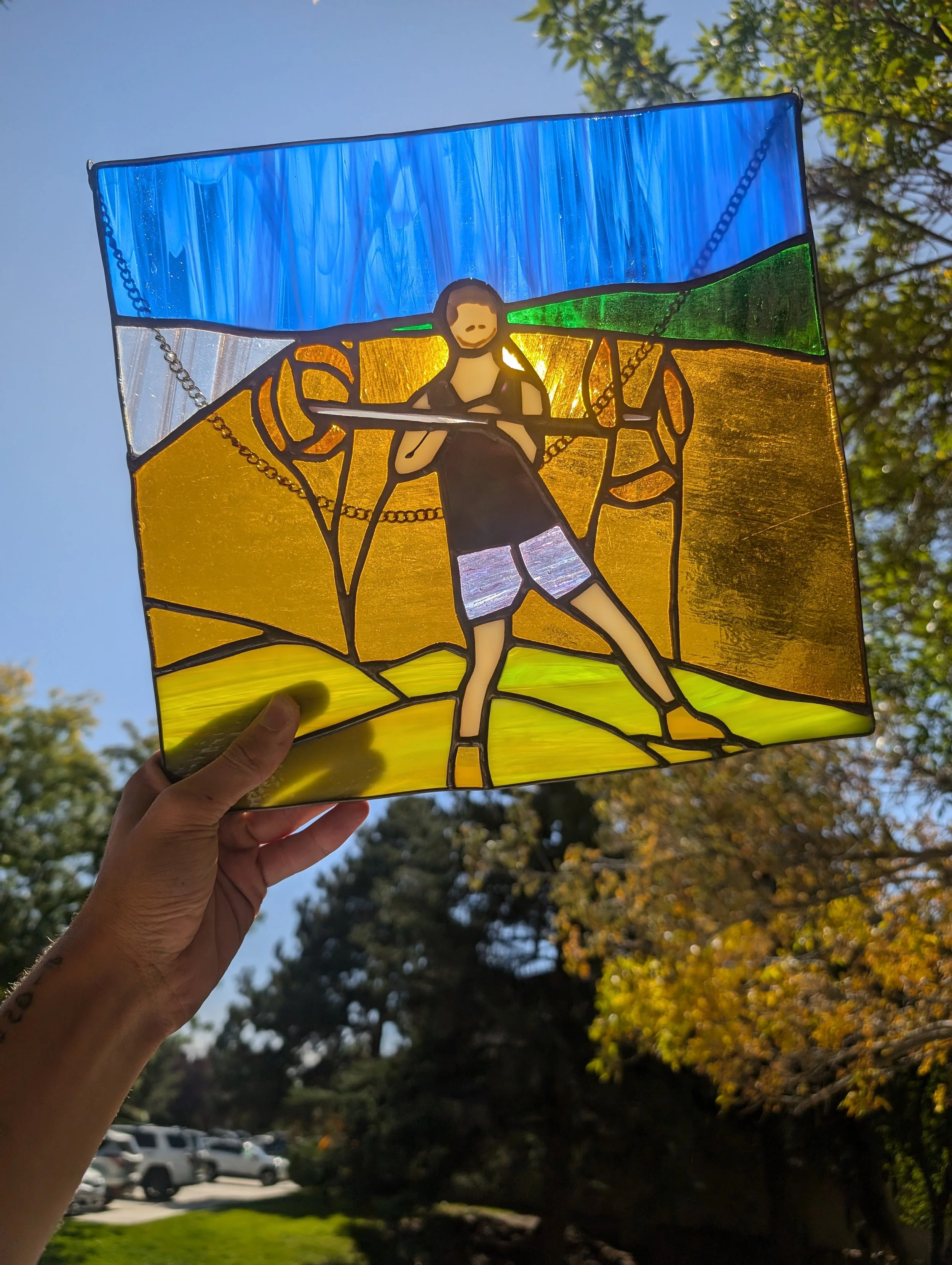 Stained glass window depicting a man with a beard and athletic clothing carrying a pole, standing in a landscape with green fields and blue sky.