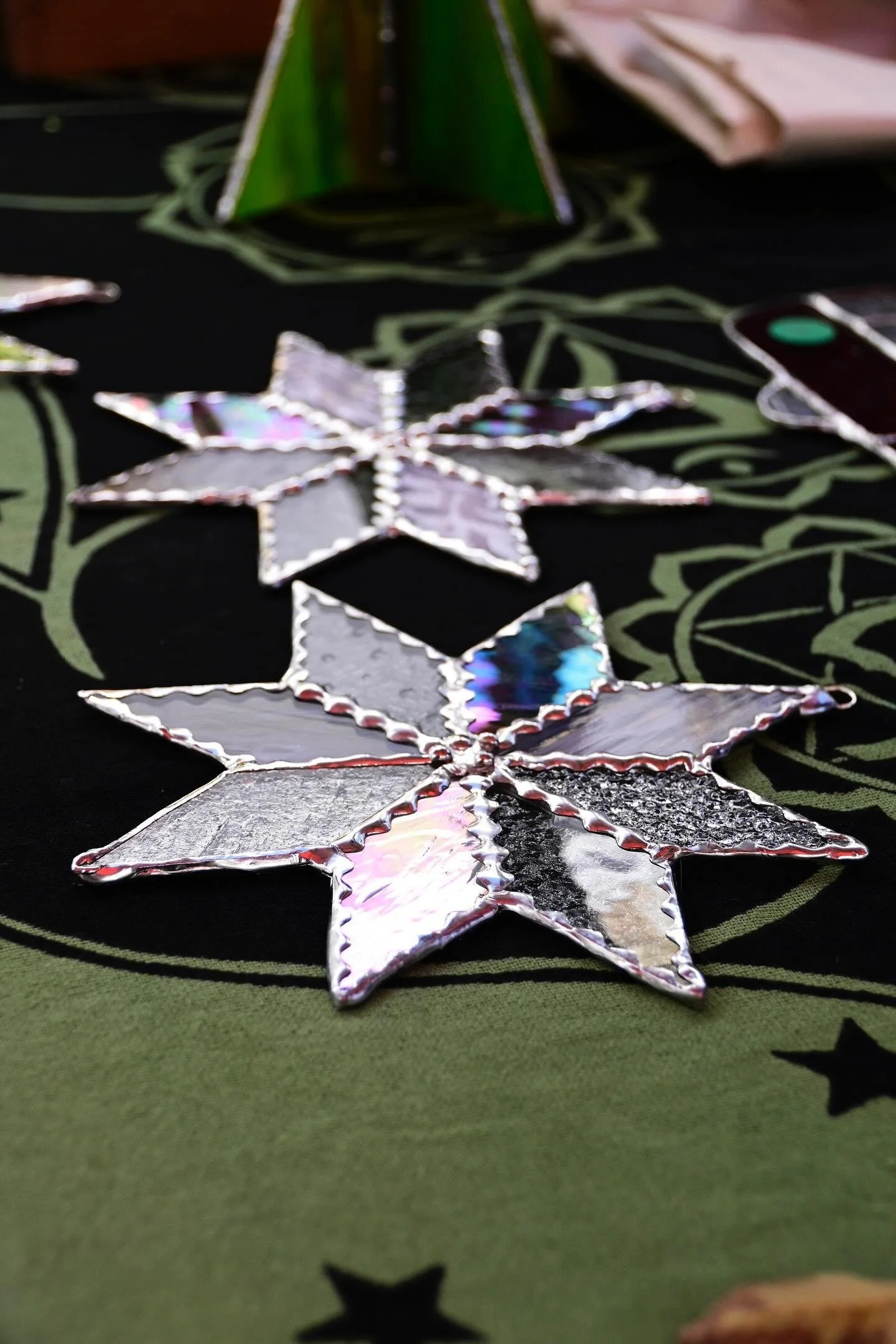 Handmade stained glass stars on a black and green fabric surface displayed at an outdoor event.