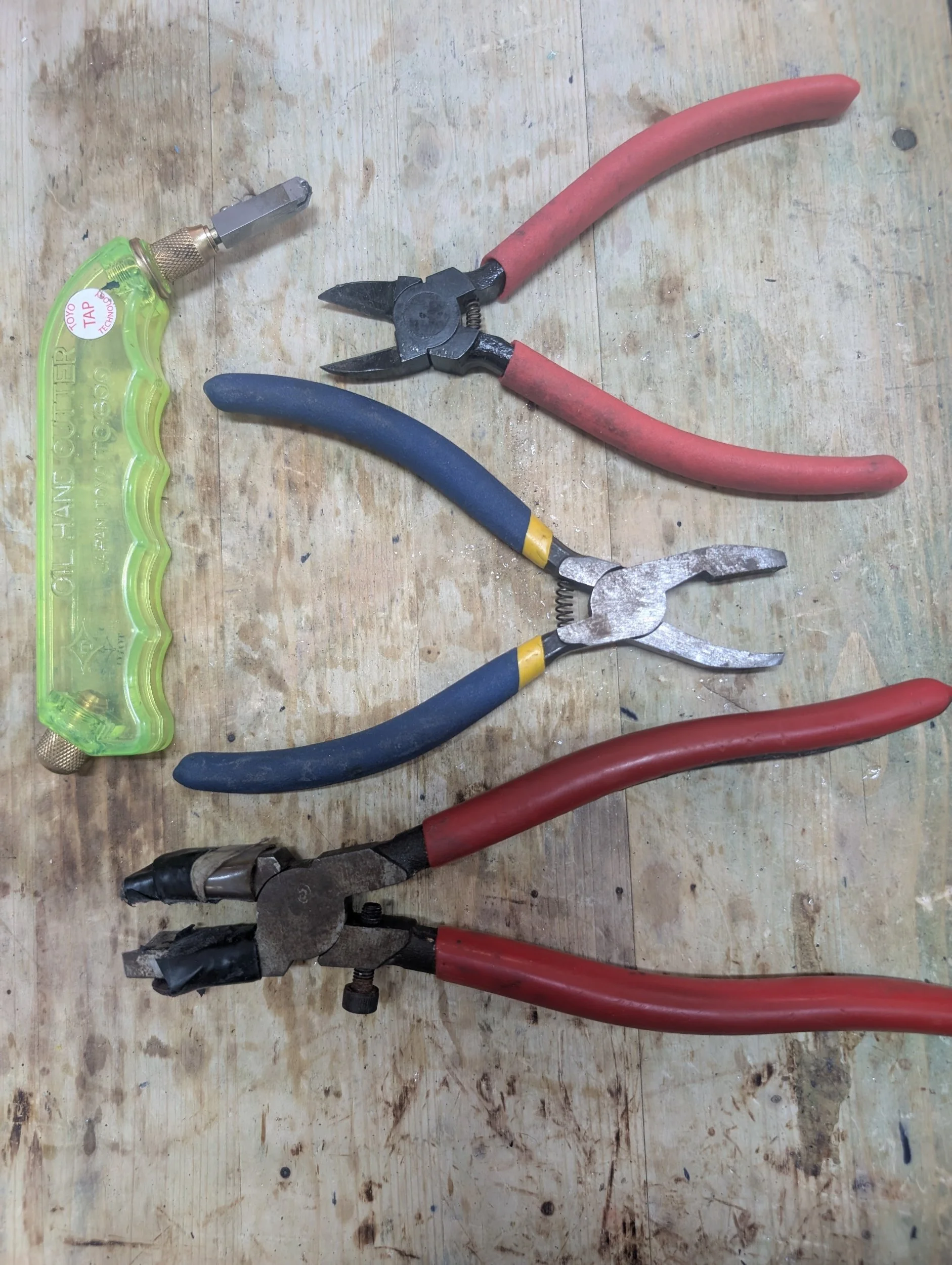 A set of three different pliers and a wire stripper tool on a wooden work surface.