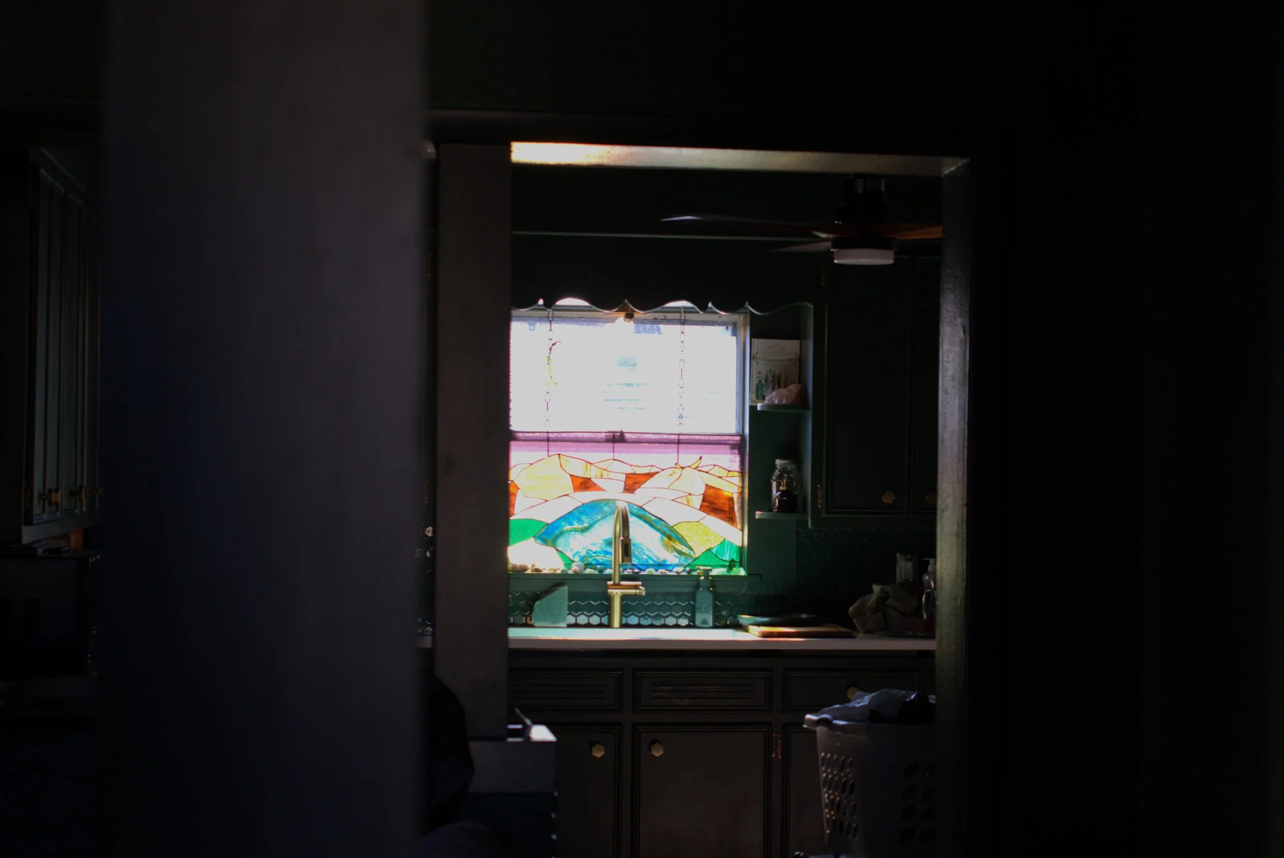 A dark kitchen with a stained-glass window above the sink, illuminated by natural light.
