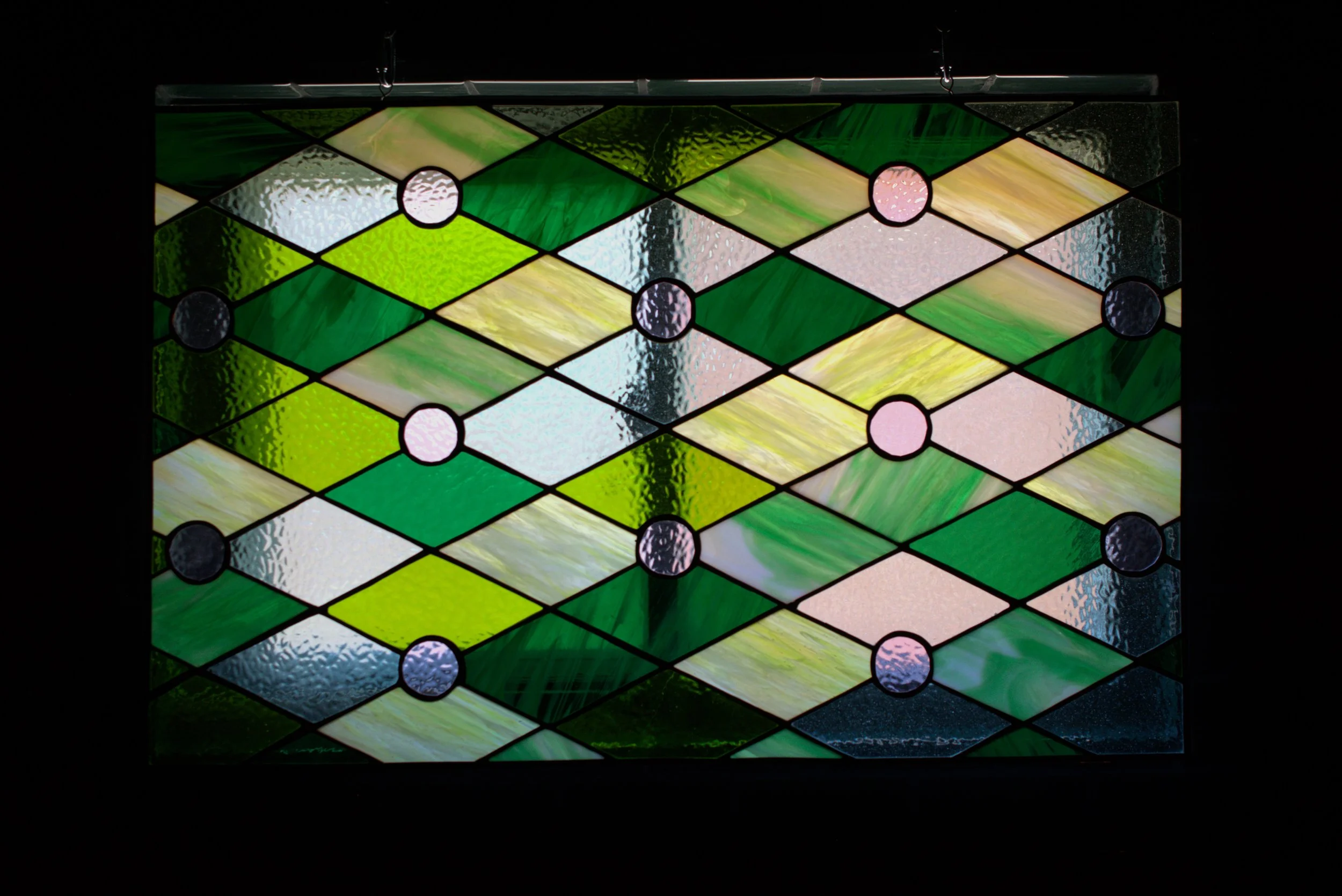 Colorful stained glass window with diamond and circle shapes in various shades of green, pink, white, and blue.