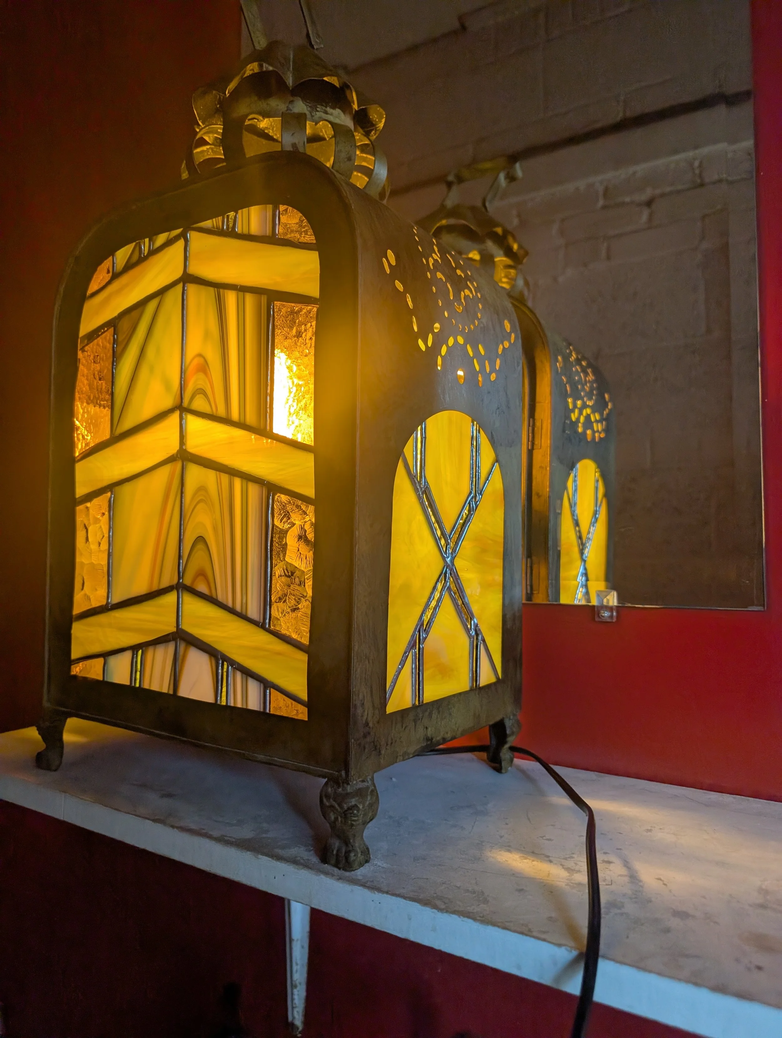 Vintage stained glass table lamp with yellow and amber hues on a white surface against a brick wall.