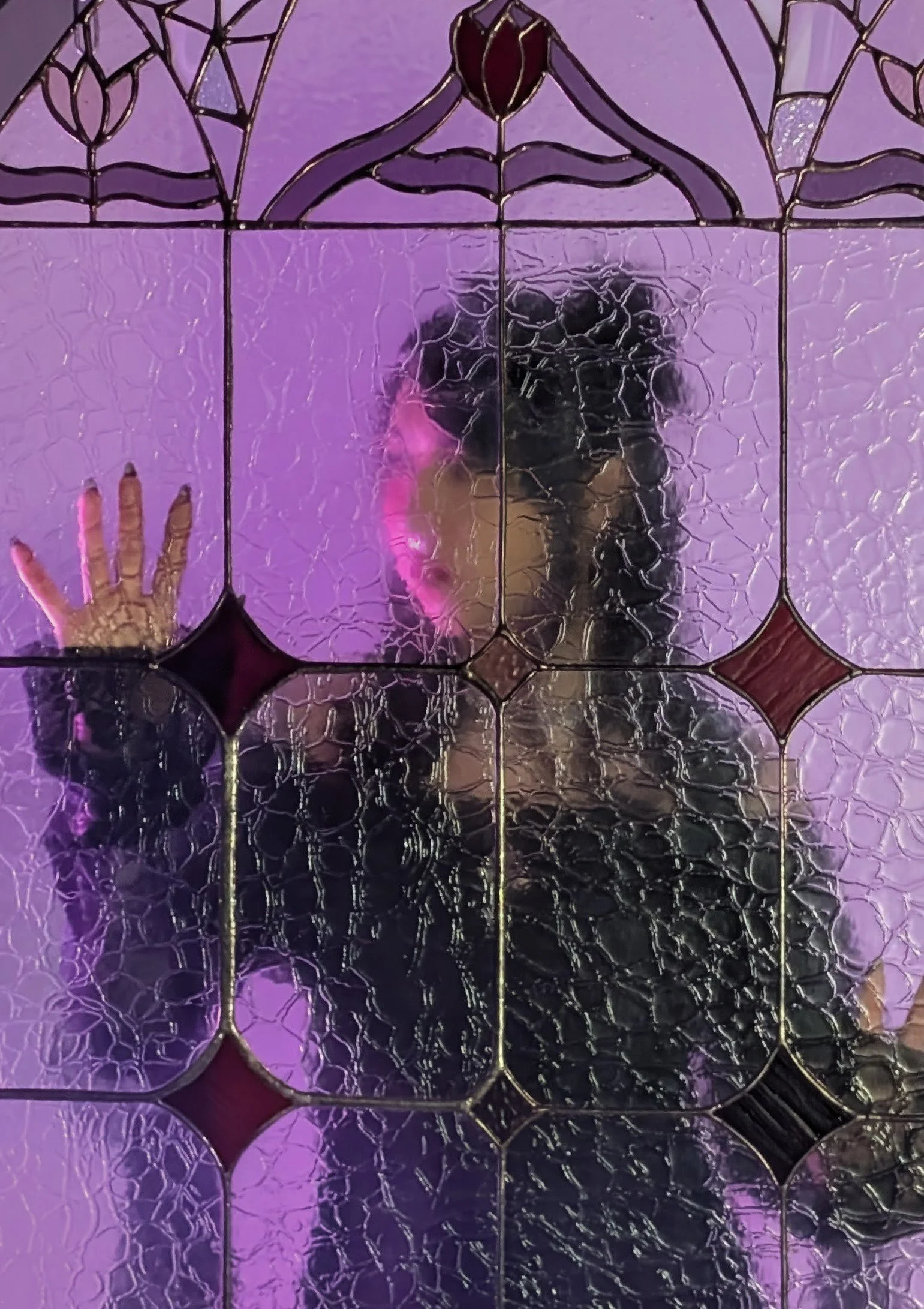 A person taking a photo through a decorative glass mirror with a cracked pattern, with purple and pink lighting in the background.