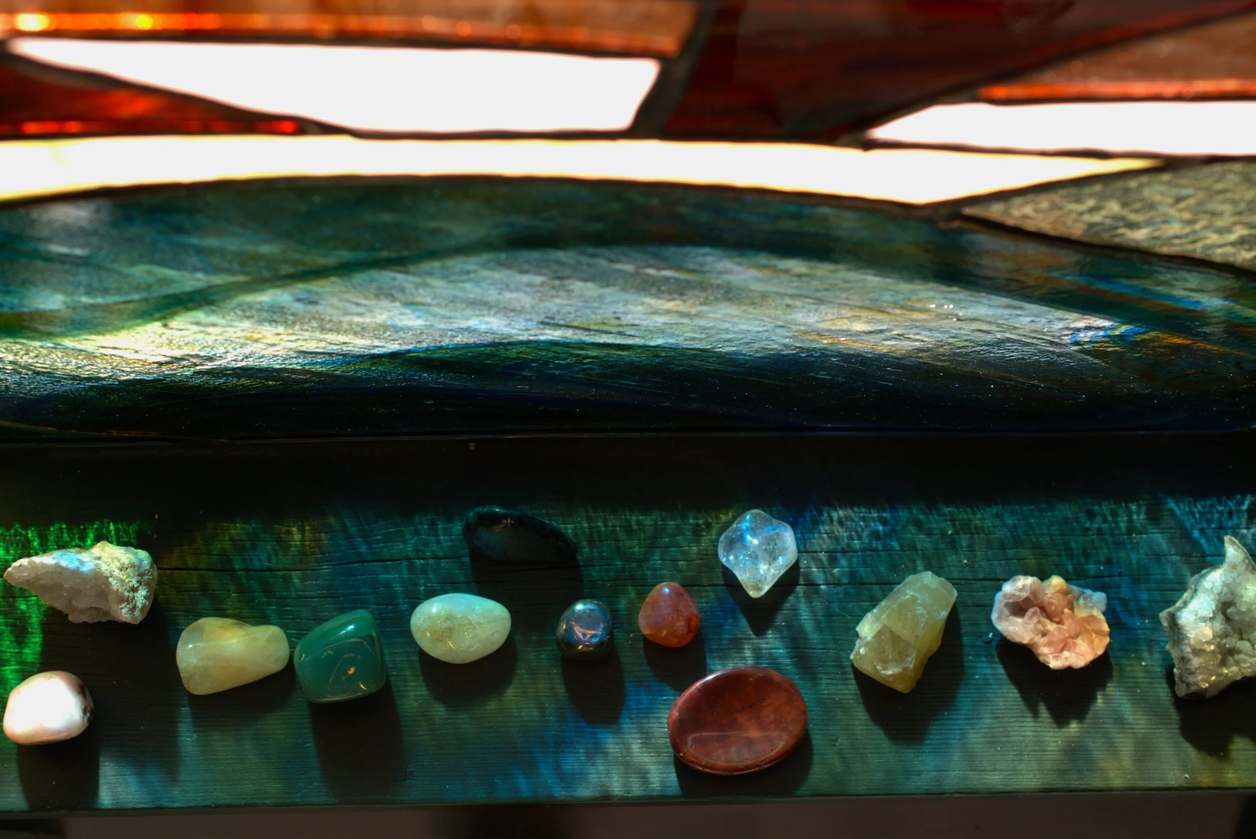 Collection of polished and raw semi-precious stones and minerals displayed on a surface with light reflections.