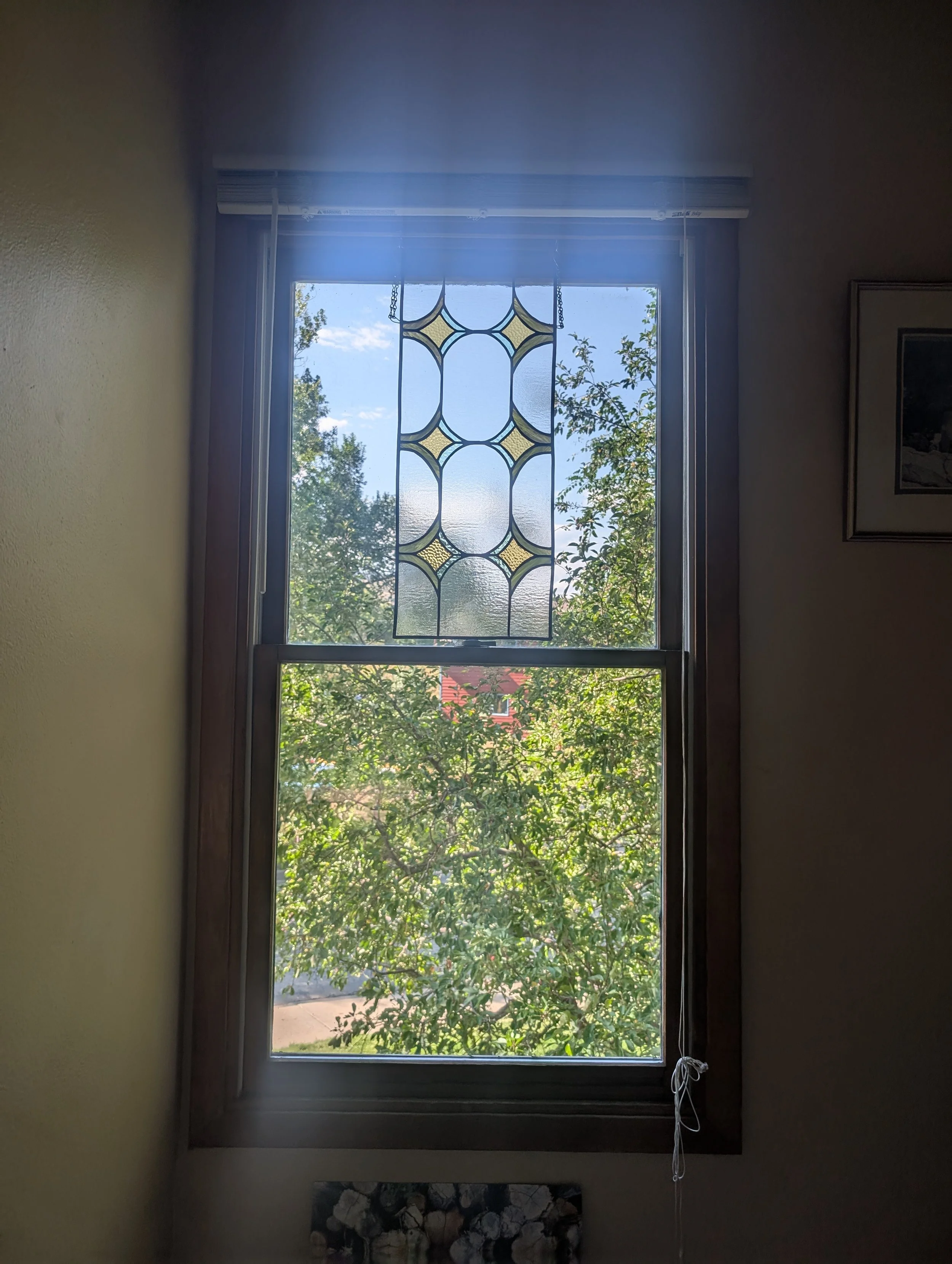 Interior view of a window with decorative stained glass at the top, showing trees and a blue sky outside.